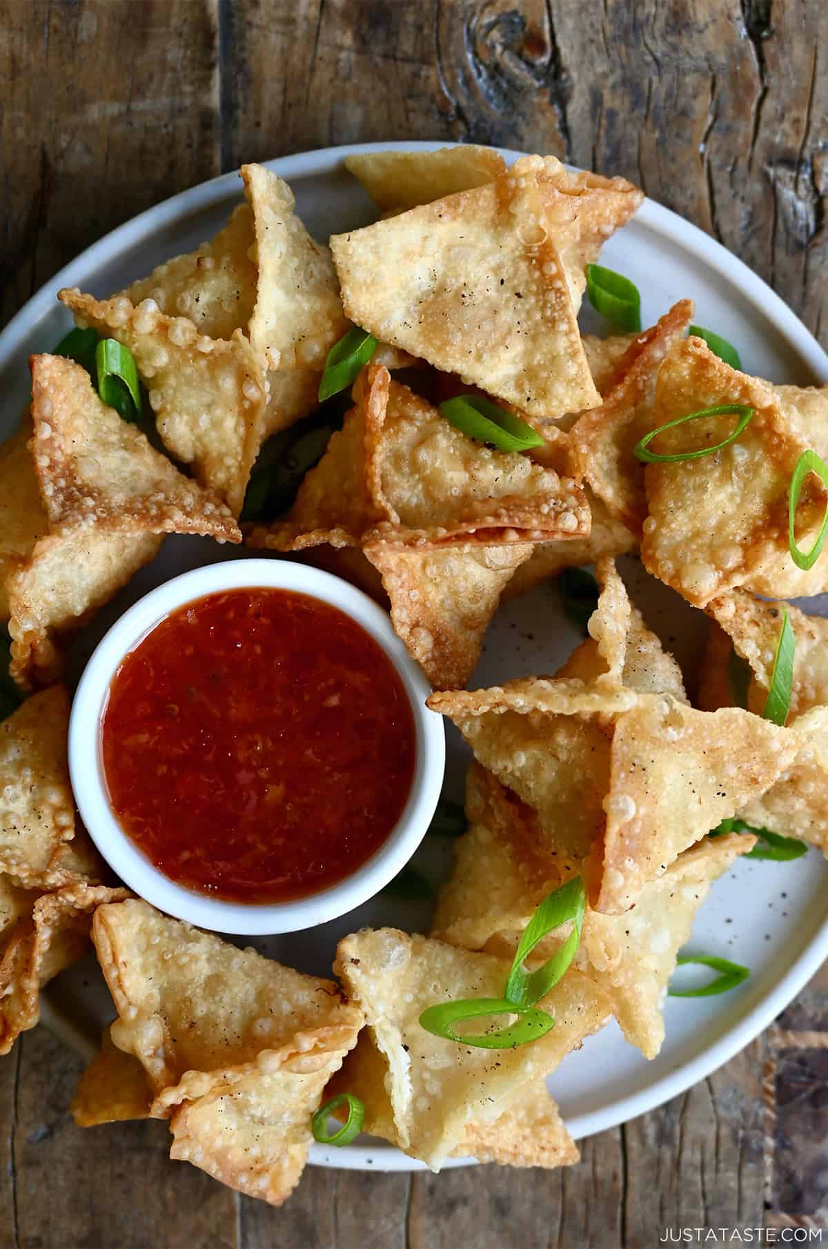 Crispy crab Rangoon on a plate with a small ramekin containing sweet and sour sauce.