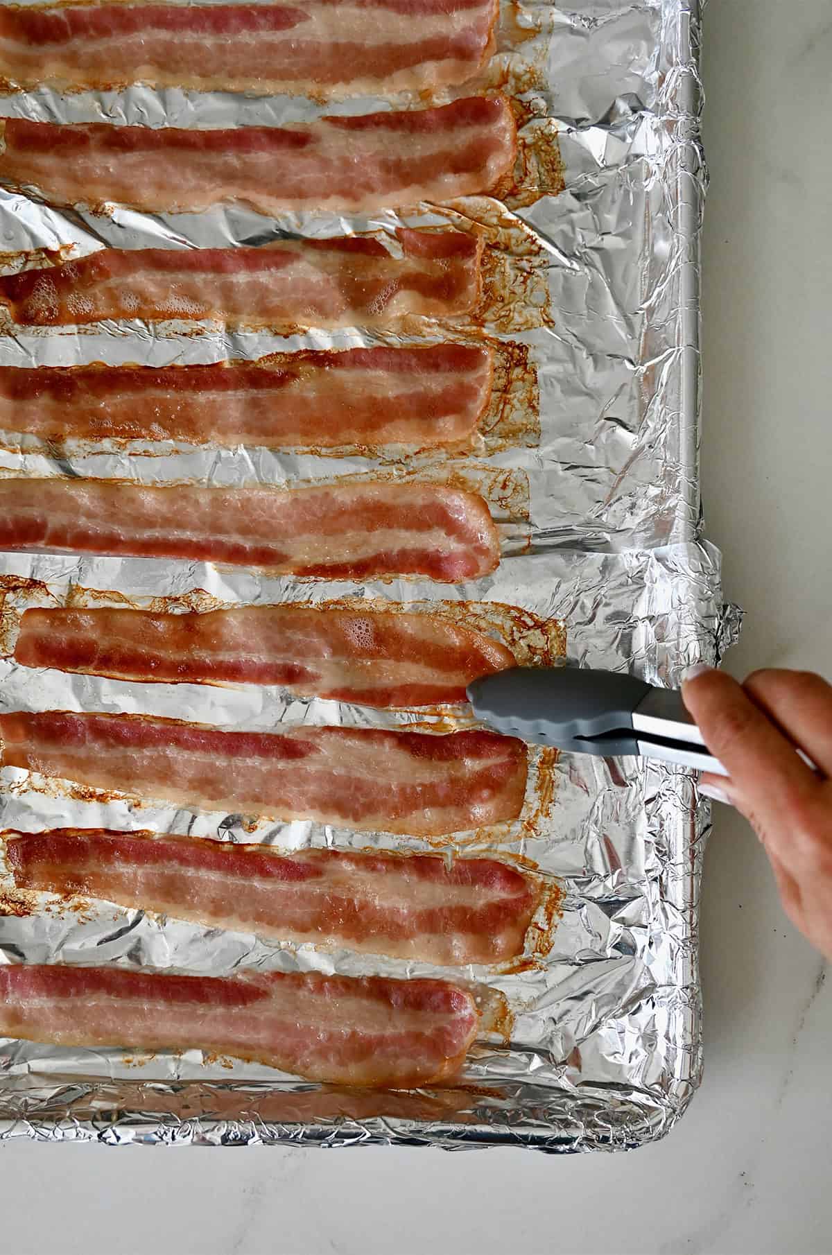 Flipping oven-baked bacon on a sheet pan.