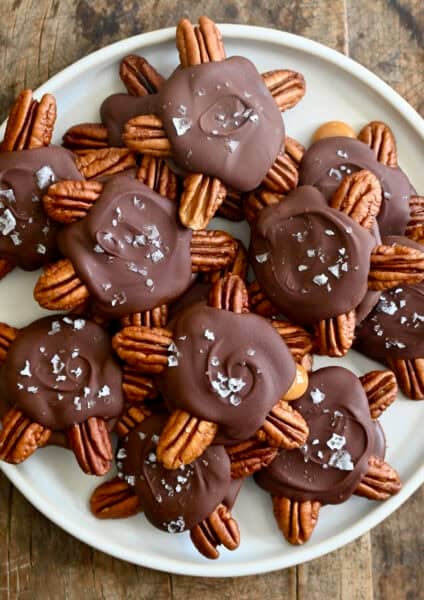 Homemade turtle candies topped with flaky sea salt on a white plate.