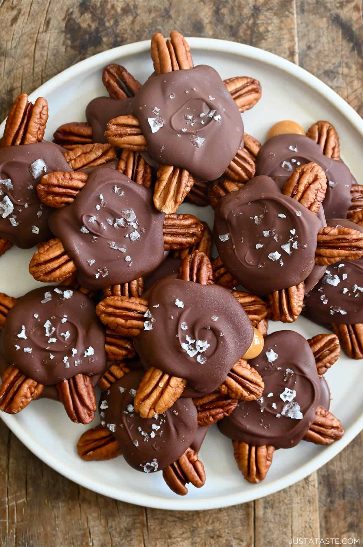 Homemade turtle candies topped with flaky sea salt on a white plate.