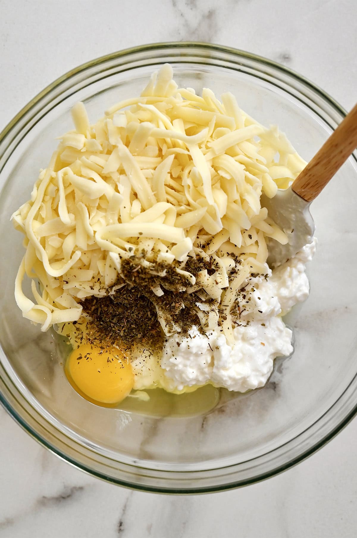 A bowl containing cottage cheese, shredded mozzarella, an egg and Italian seasoning to make the cheesy layer of lasagna.