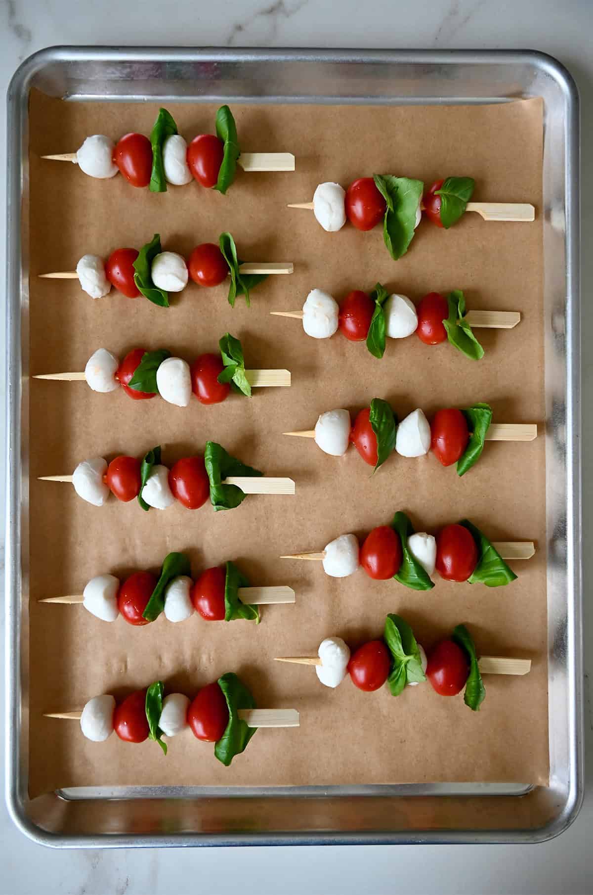 Two rows of caprese skewers on a parchment paper-lined baking sheet.