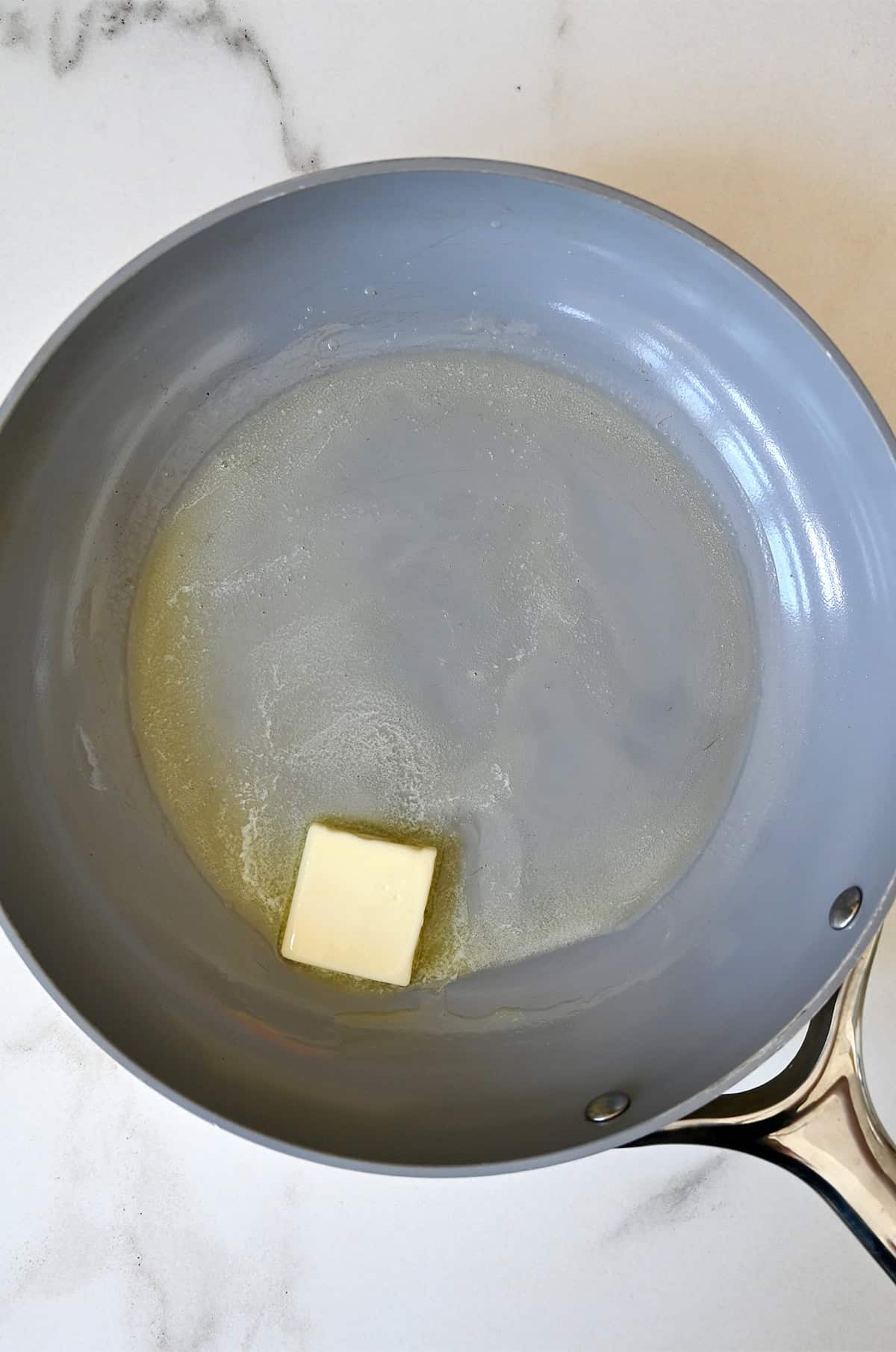 A pad of butter in a nonstick pan is just starting to melt.