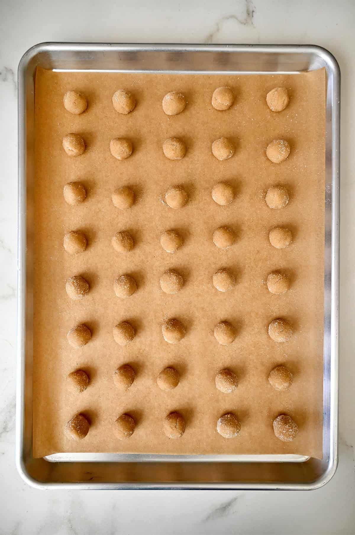 Mini peanut butter dough balls coated in sugar on a parchment paper-lined baking sheet.