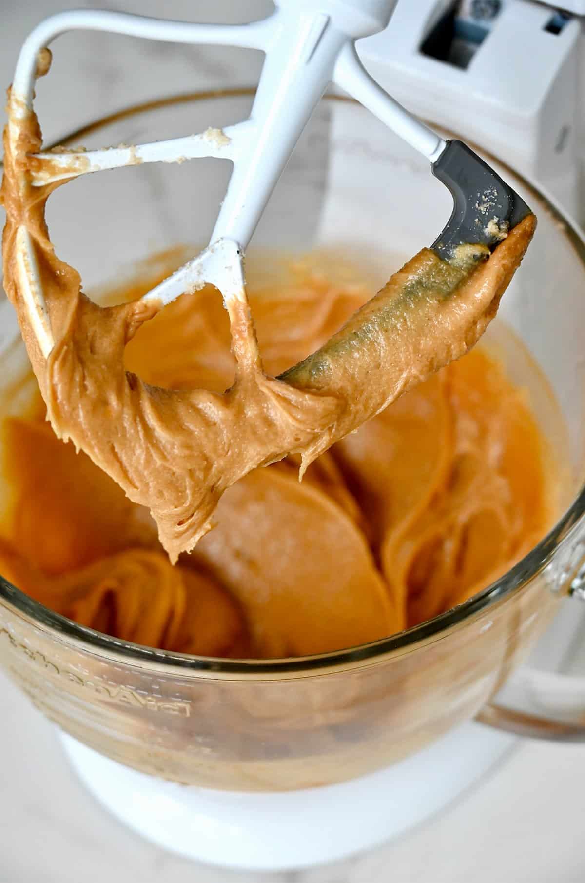 Peanut butter mixed with creamed butter, sugars, vanilla extract and eggs in the bowl of a stand mixer.