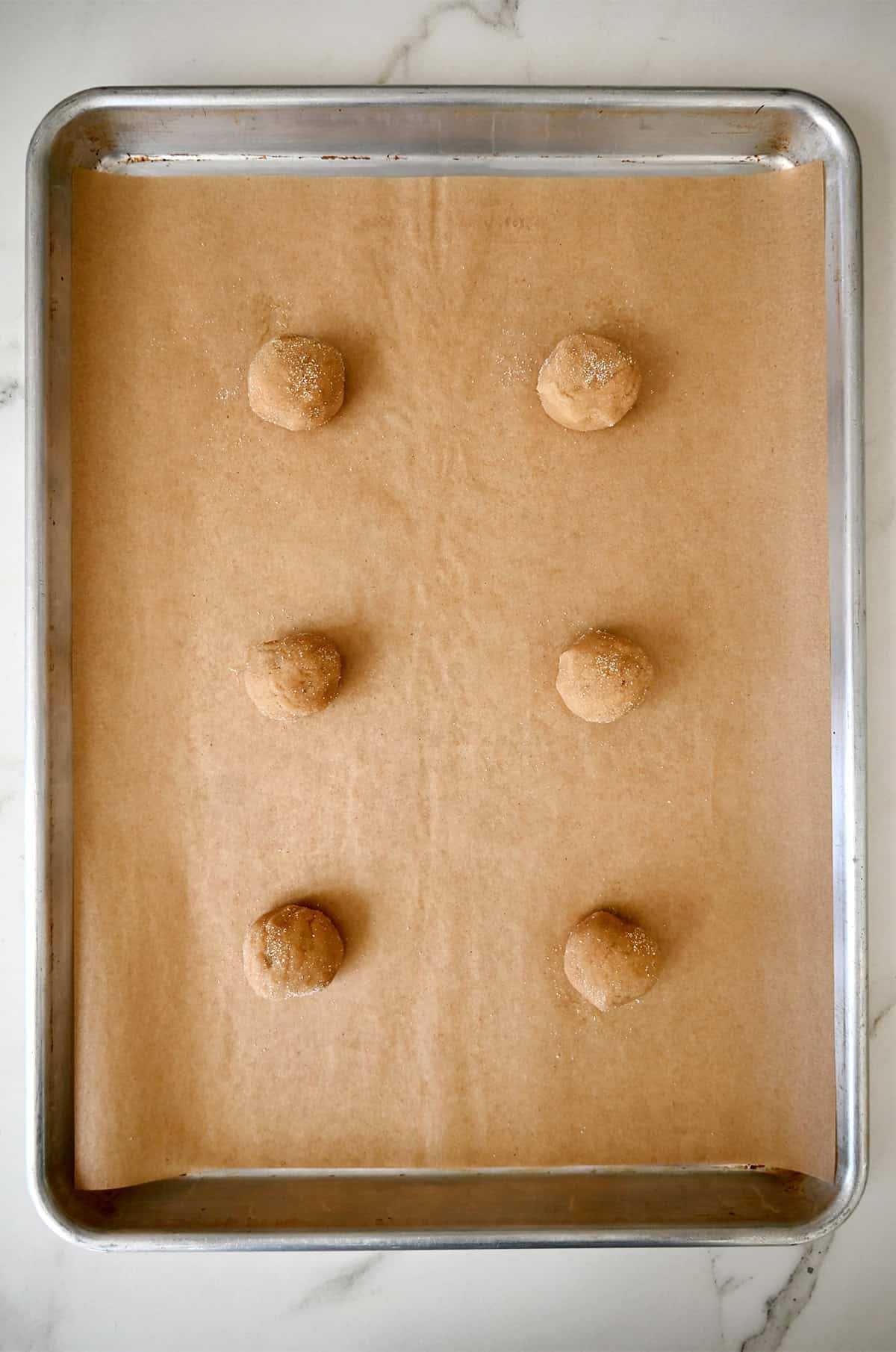 Peanut butter dough balls coated in sugar on a baking sheet lined with parchment paper.