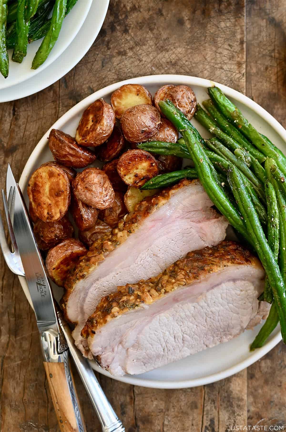 Roasted pork loin slices on a dinner plate with roasted potatoes and green beans.