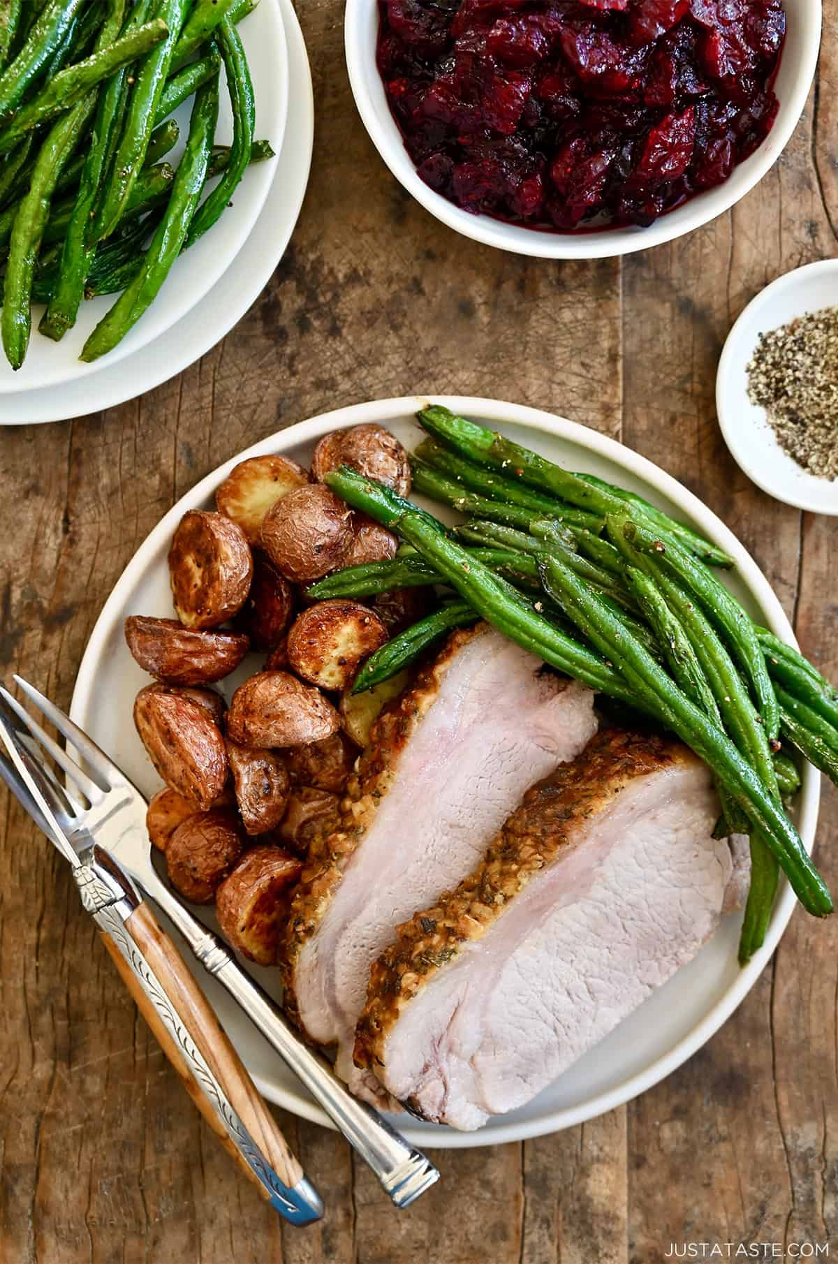 Two slices of herb-crusted pork loin roast on a dinner plate with roasted green beans and potatoes.