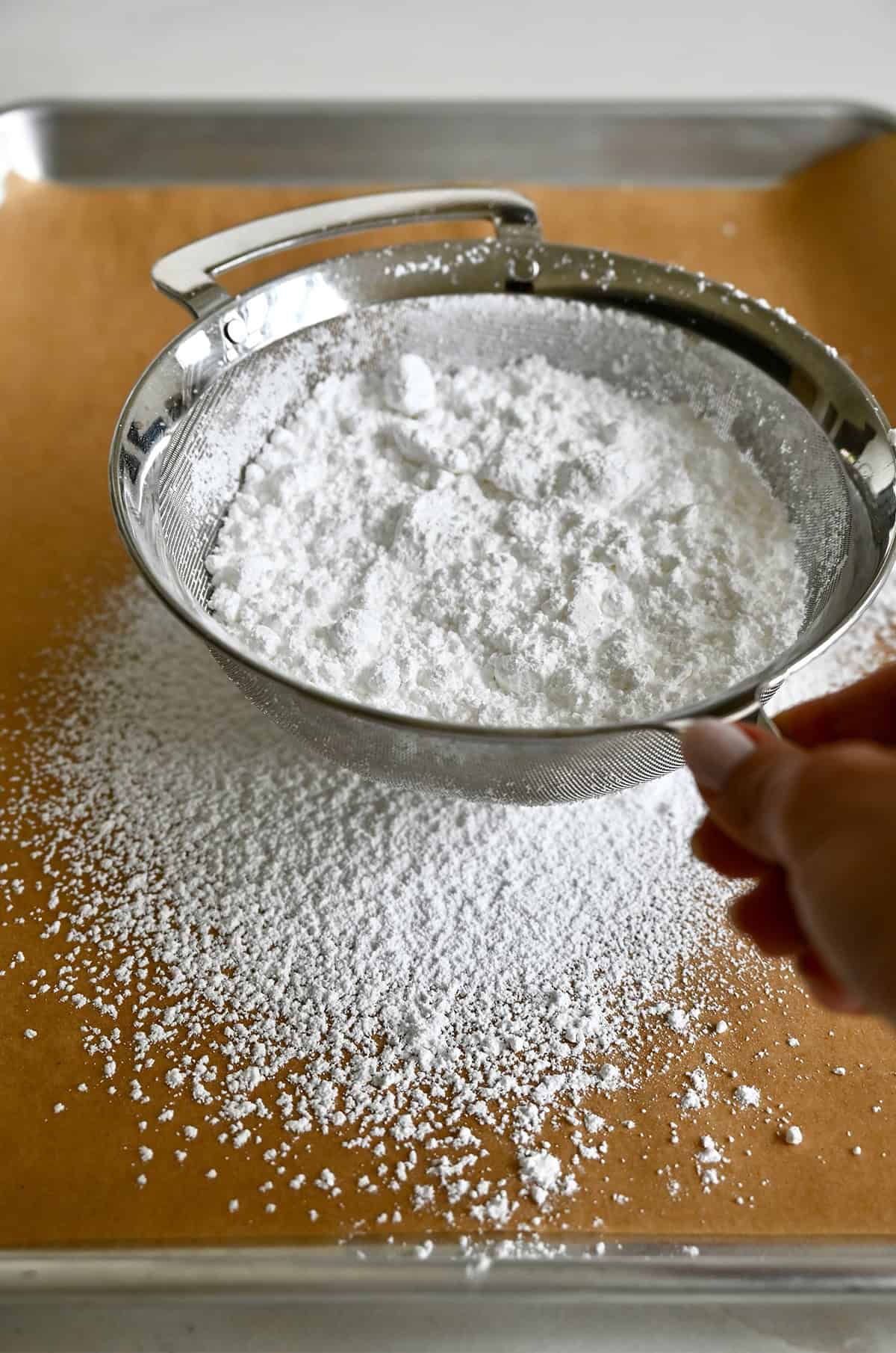 Sifting powdered sugar from a sieve onto parchment paper.