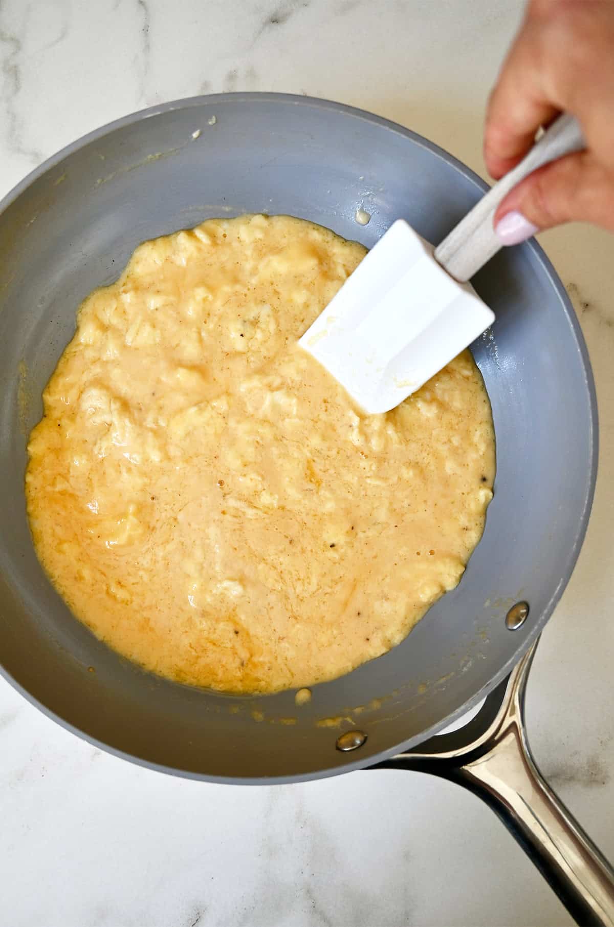 Using a flexible silicone spatula to soft scramble eggs in a nonstick skillet.