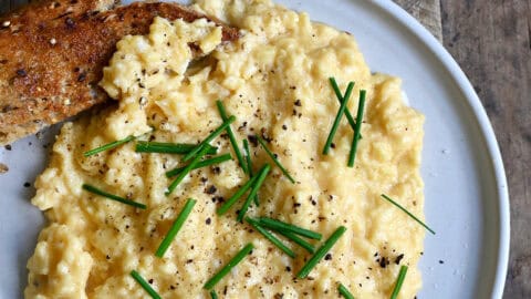 Soft scrambled eggs topped with salt, pepper and fresh chives on a plate with sourdough toast.
