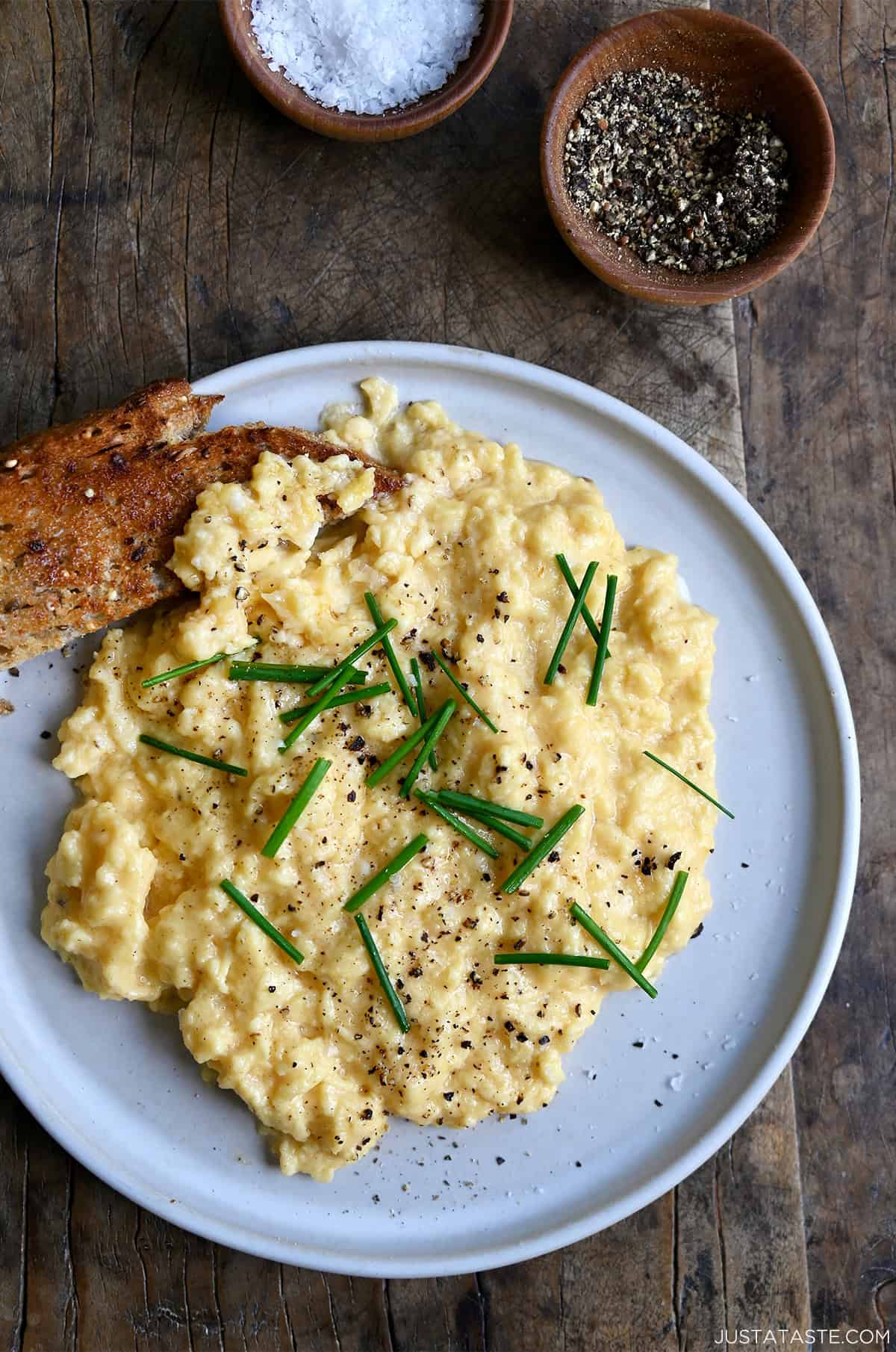 Soft scrambled eggs topped with salt, pepper and fresh chives on a plate with sourdough toast.