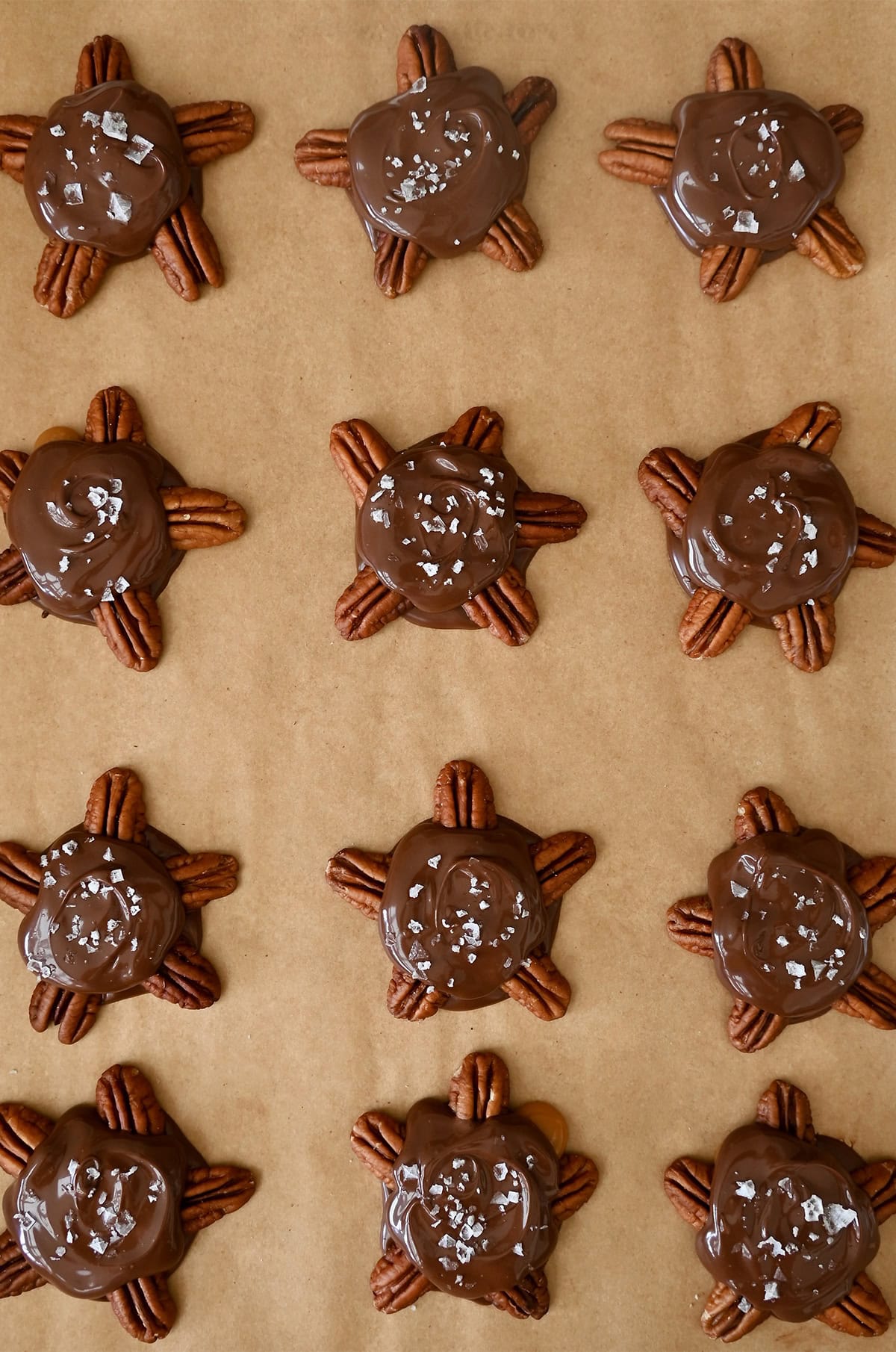 Chocolate pecan turtles topped with flaky sea salt cooling on a baking sheet.