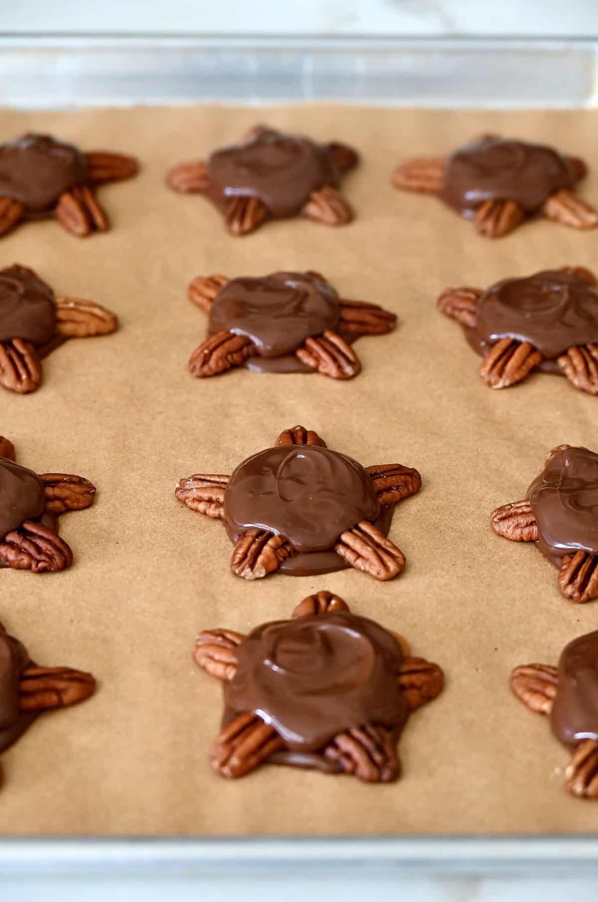 Homemade chocolate turtles on a parchment paper-lined baking sheet.