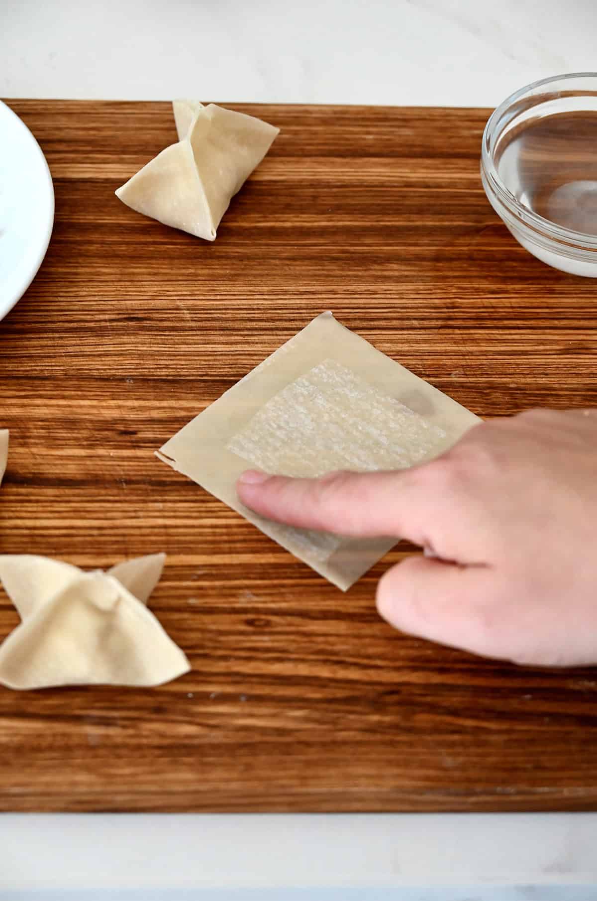 A finger lightly moistening the edges of a wonton wrapper with water.