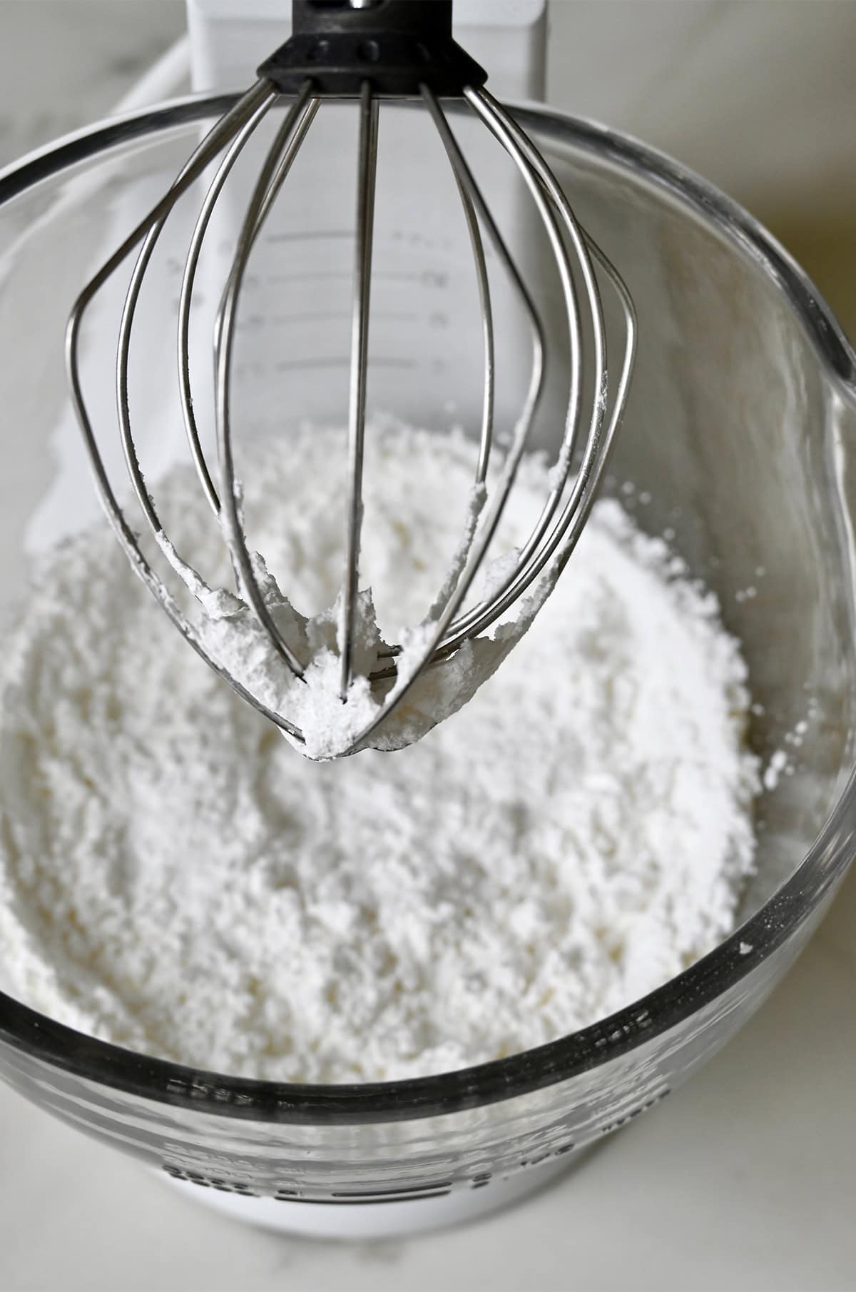 Whisking together sifted powdered sugar with merigue powder in a stand mixer with the whisk attachment.