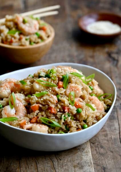Shrimp fried rice with peas and carrots in a dinner bowl with chopsticks.