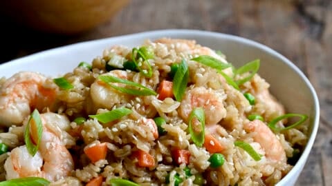 Shrimp fried rice with peas and carrots in a dinner bowl with chopsticks.