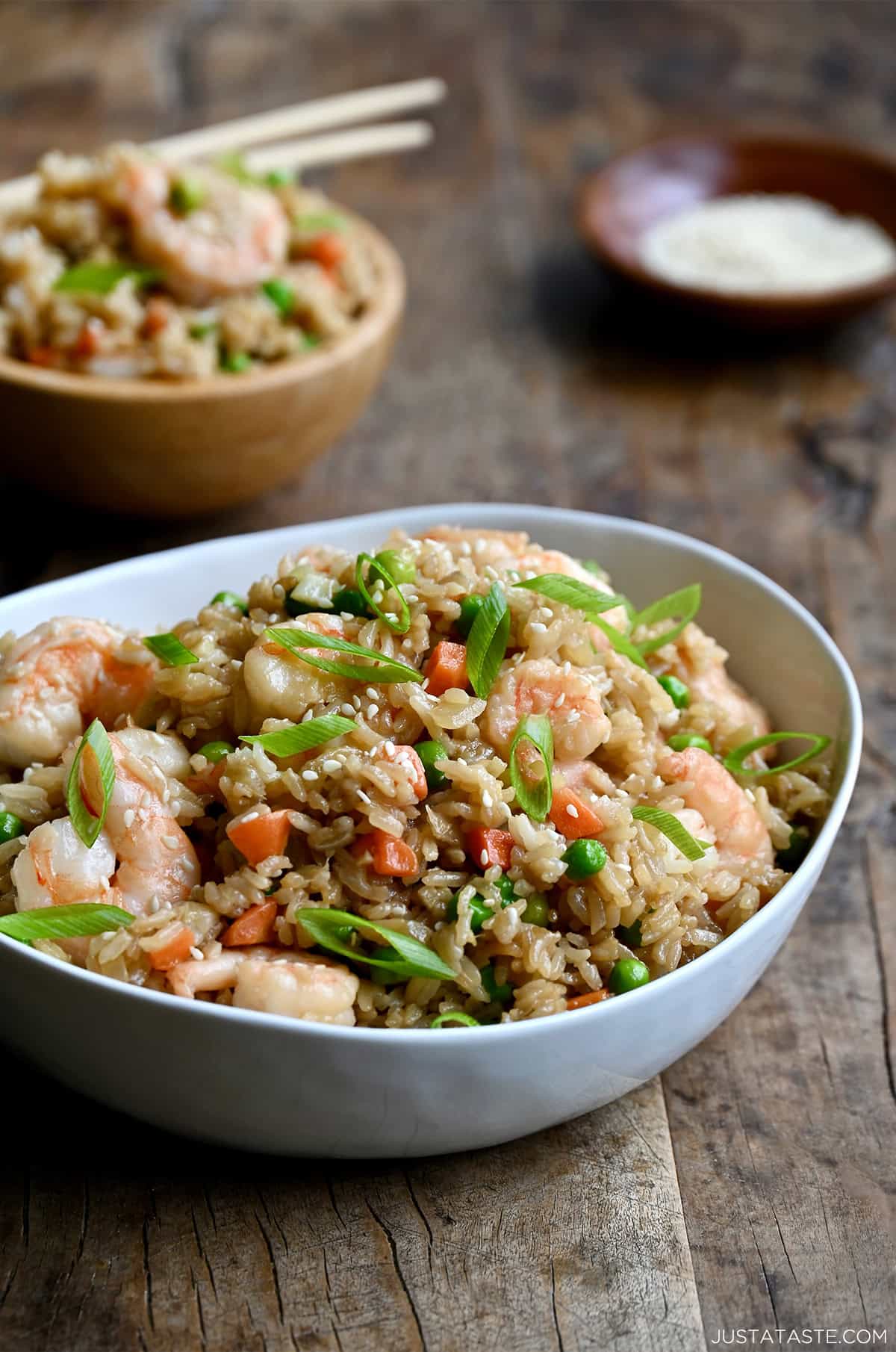 Shrimp fried rice with peas and carrots in a dinner bowl with chopsticks.