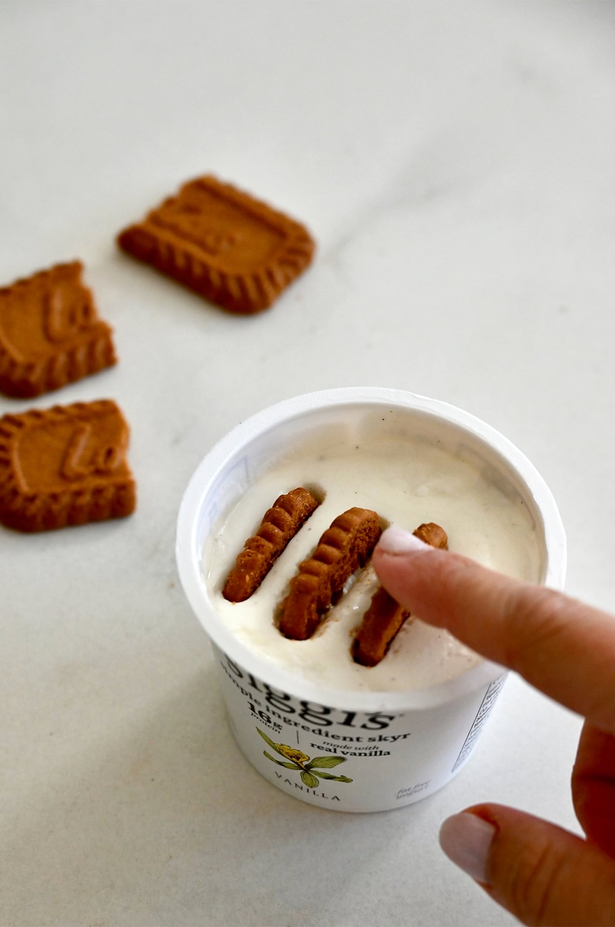 Adding halved Biscoff cookies to a single serving cup of Greek yogurt.