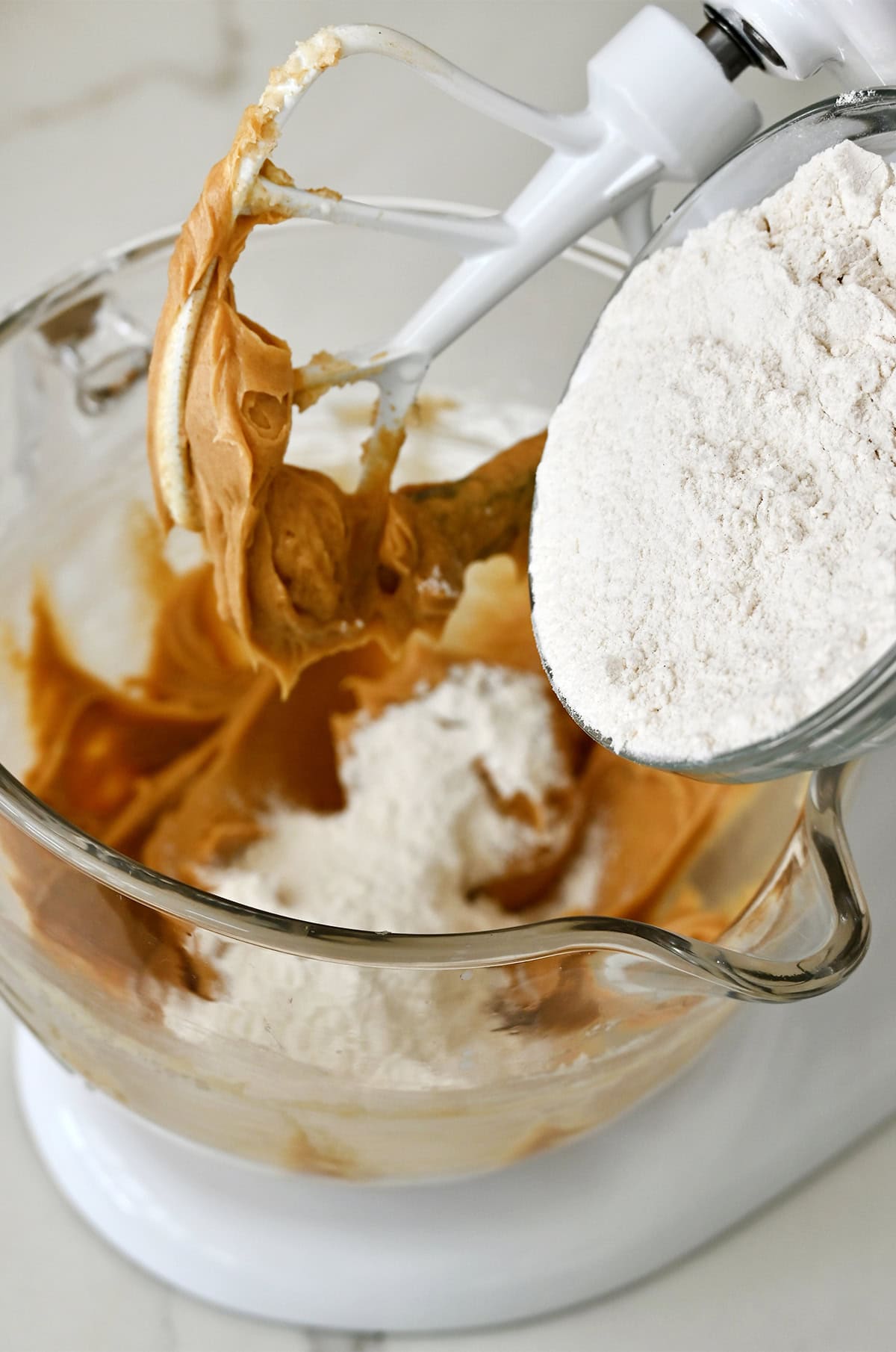 Adding flour mixture to a bowl with creamed butter, sugars and peanut butter.