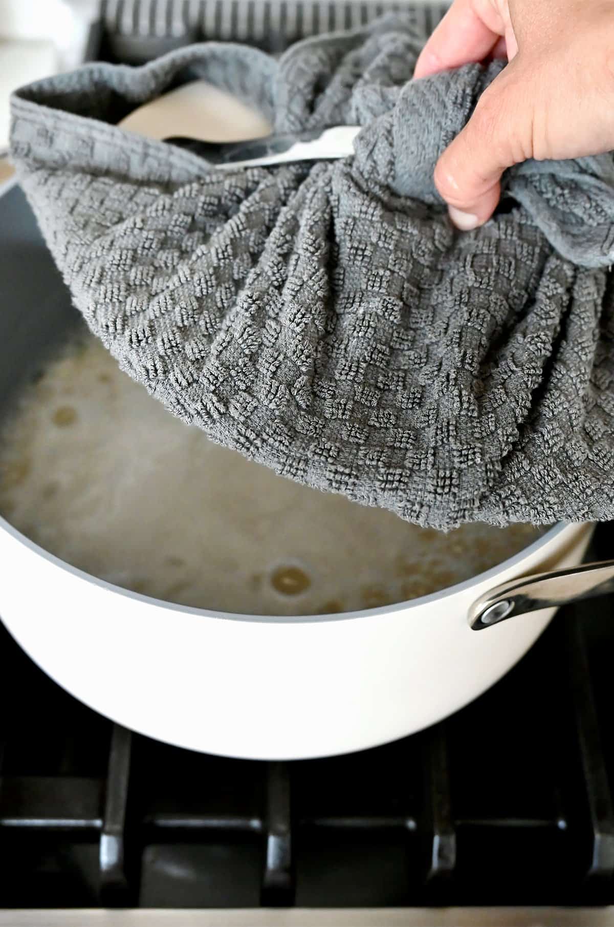 Placing a towel-wrapped lid atop a saucepan containing rice and water.
