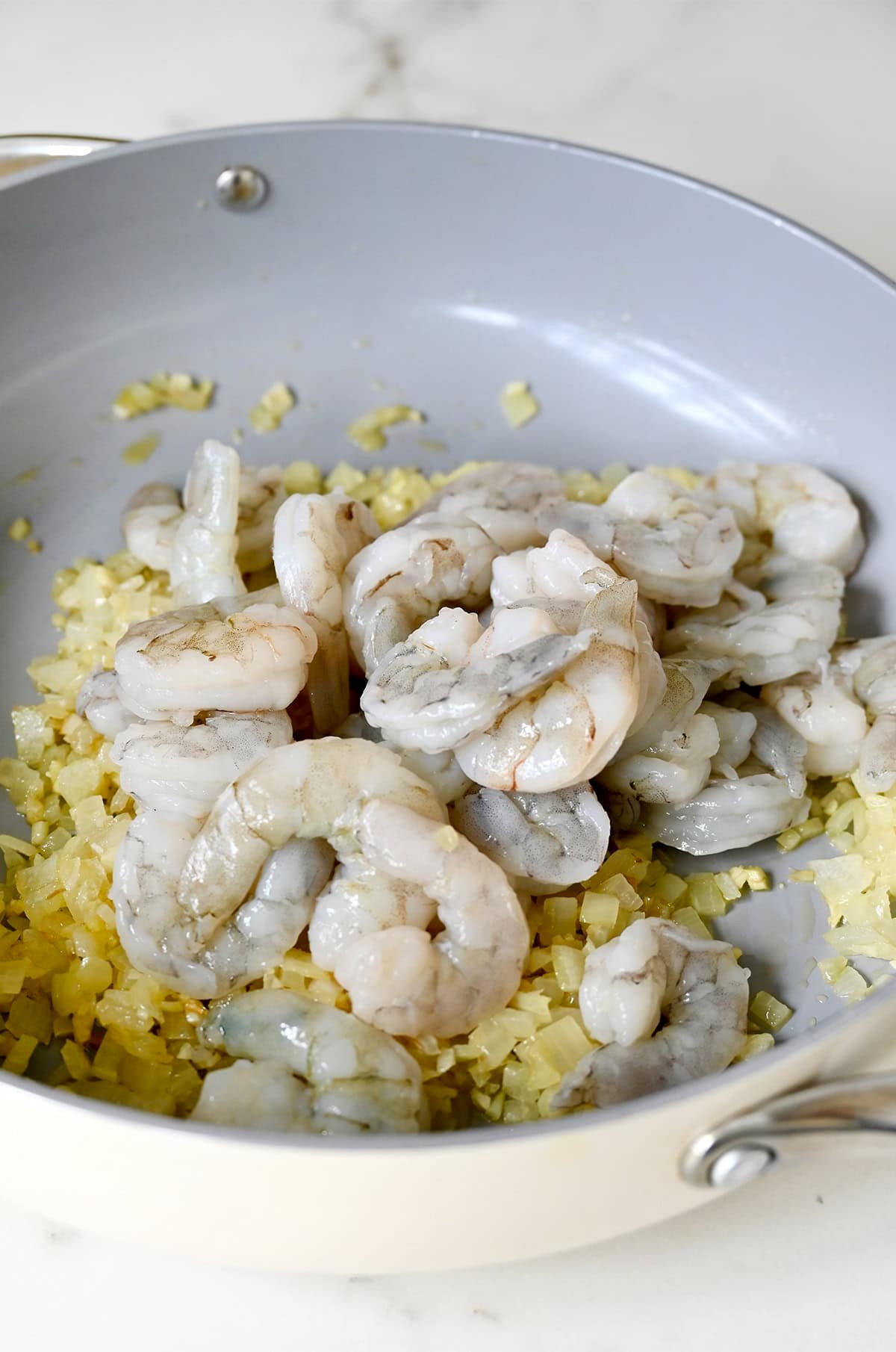 Raw shrimp in a large skillet with sauteed onions, garlic and ginger.