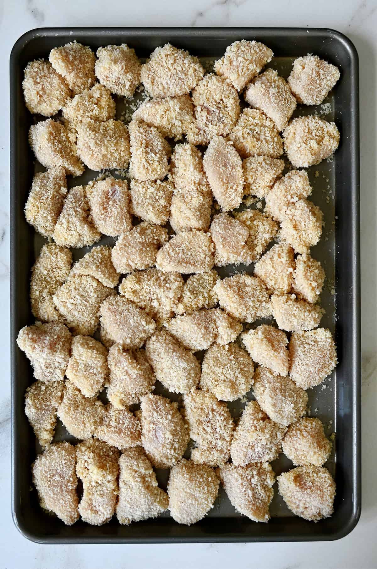Panko breaded chicken pieces on a baking sheet before deep-frying.