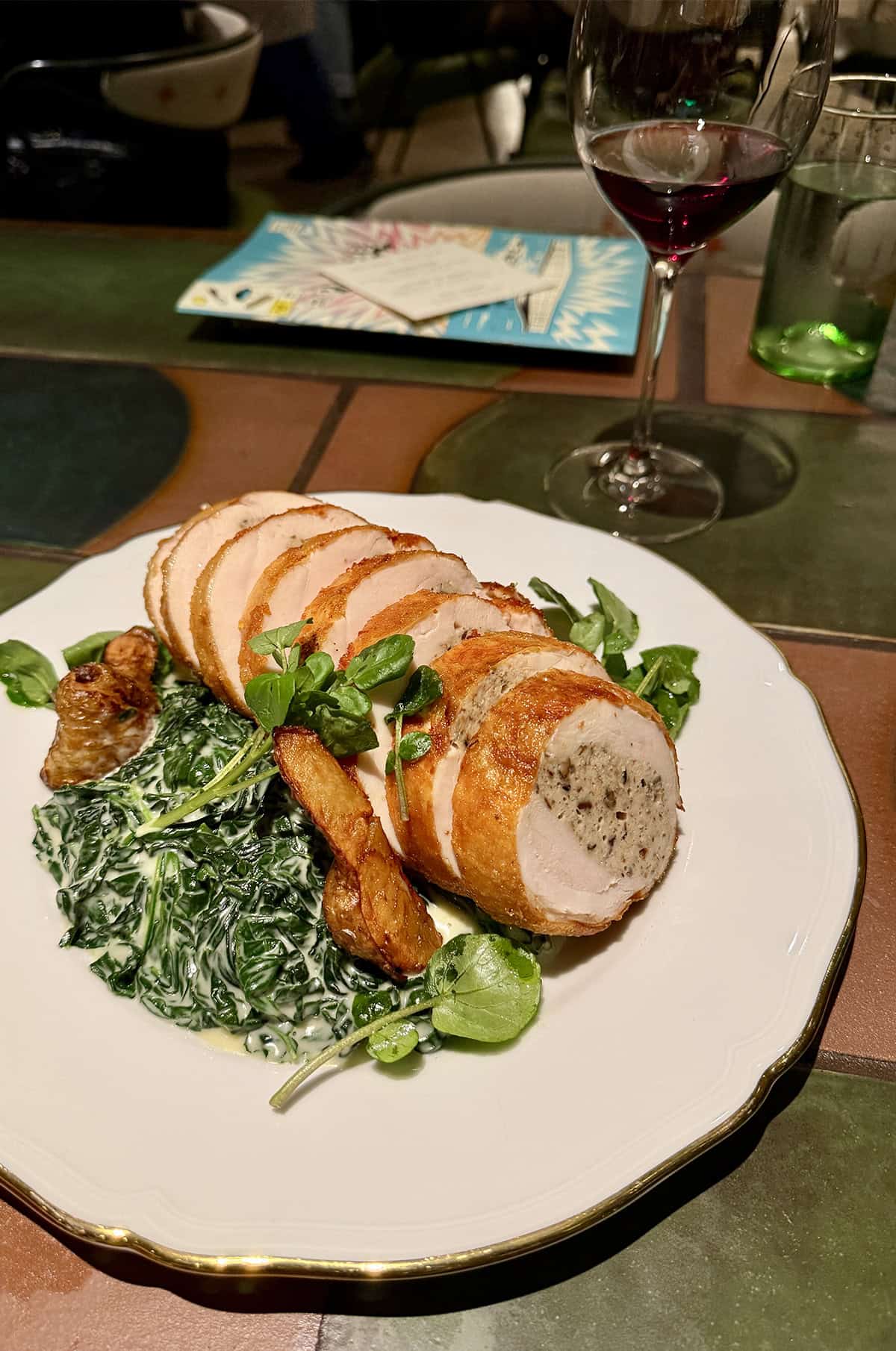 A white plate containing chicken ballotine with creamed spinach