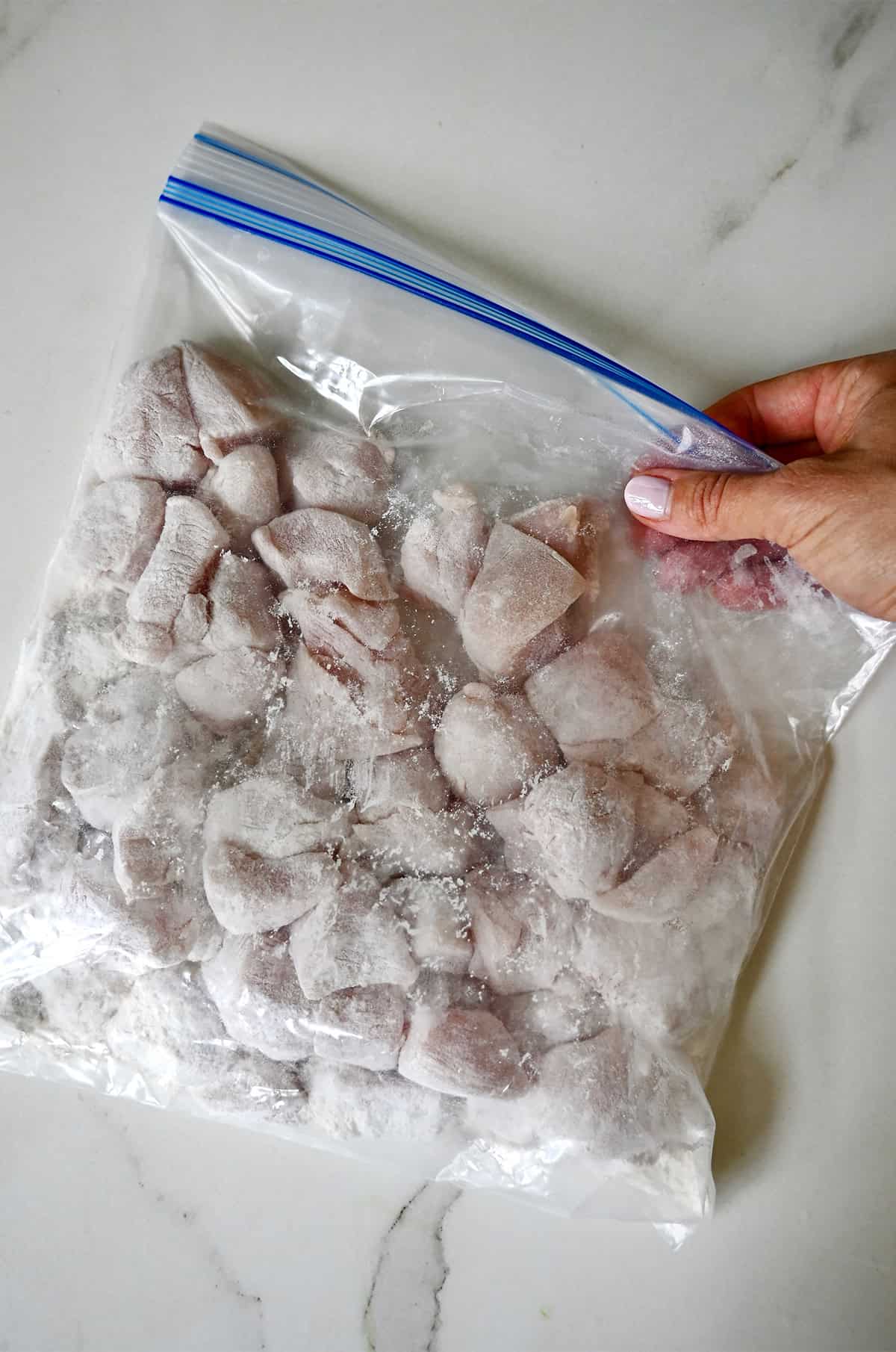 Coating chicken breast pieces in flour in a resealable plastic bag.