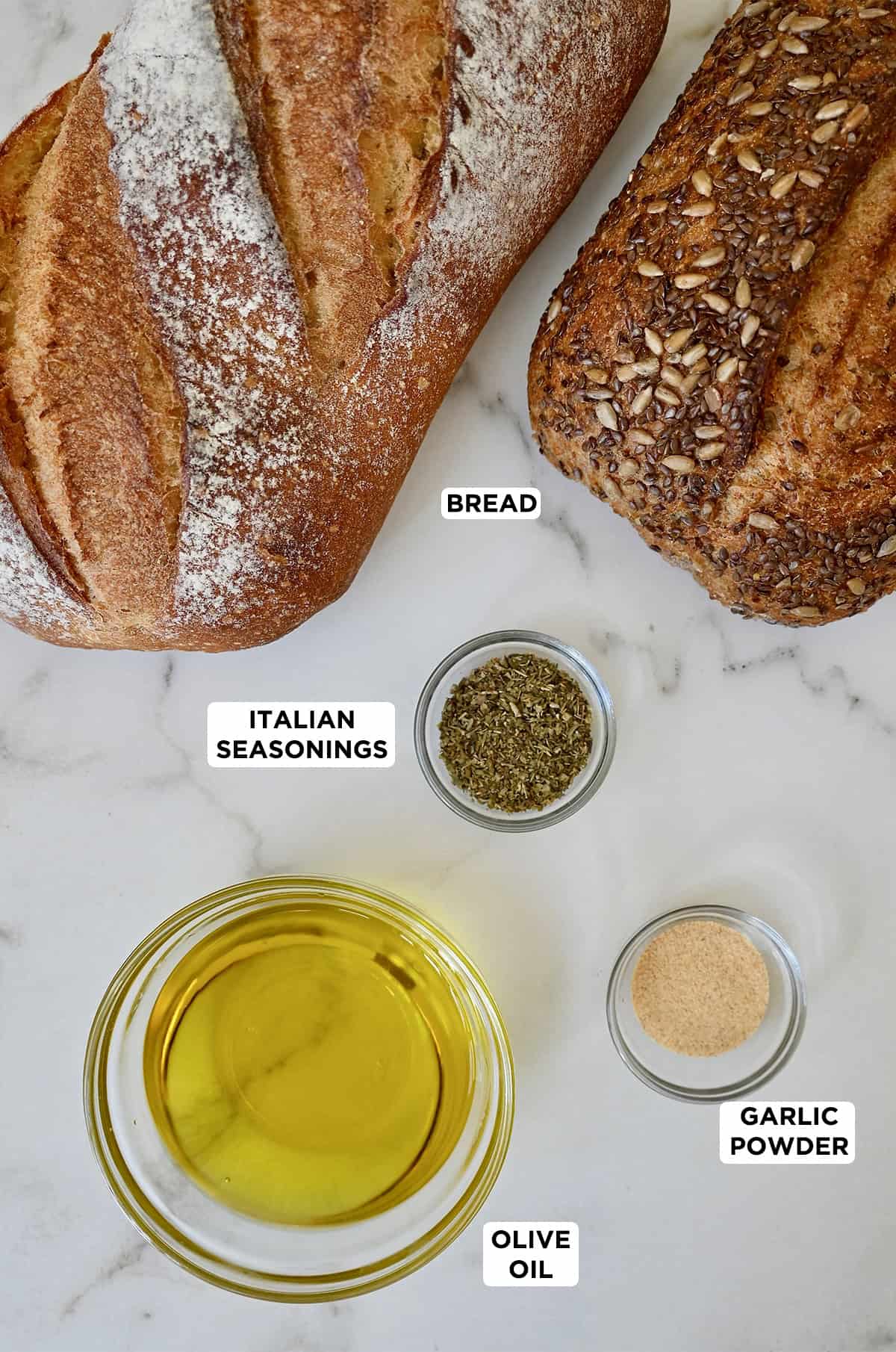Ingredients to make croutons, including a loaf of crusty bread, olive oil, Italian seasonings and garlic powder.