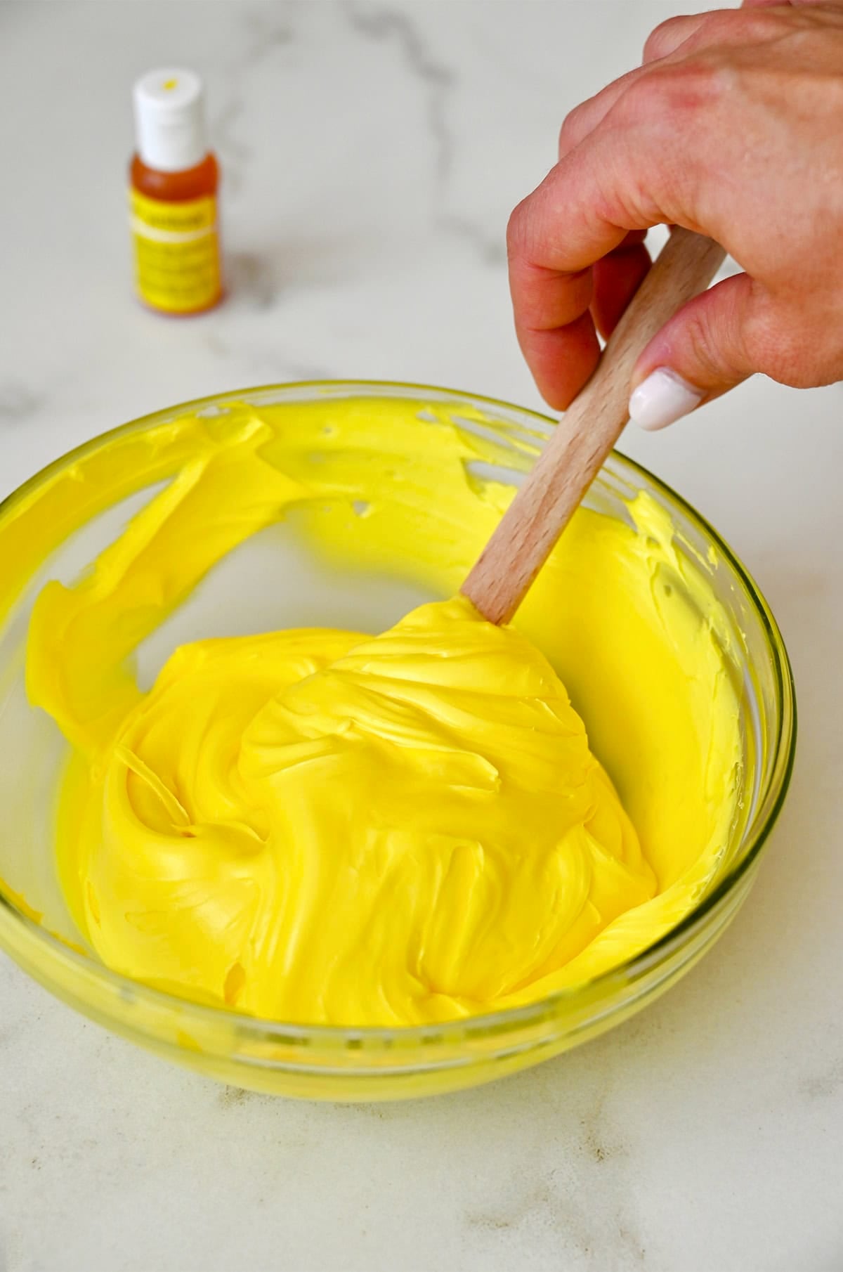 Using gel food coloring to dye vanilla buttercream yellow.