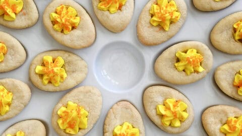 Soft sugar cookie cups decorated to look like deviled eggs, filled with buttercream frosting and finished with orange sanding sugar.
