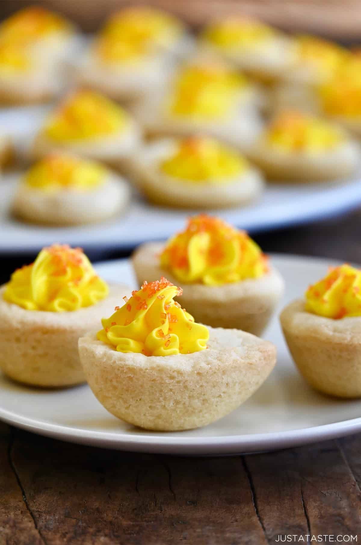 Sugar cookie cups filled with yellow buttercream frosting and sprinkled with orange sanding sugar to look like deviled eggs.
