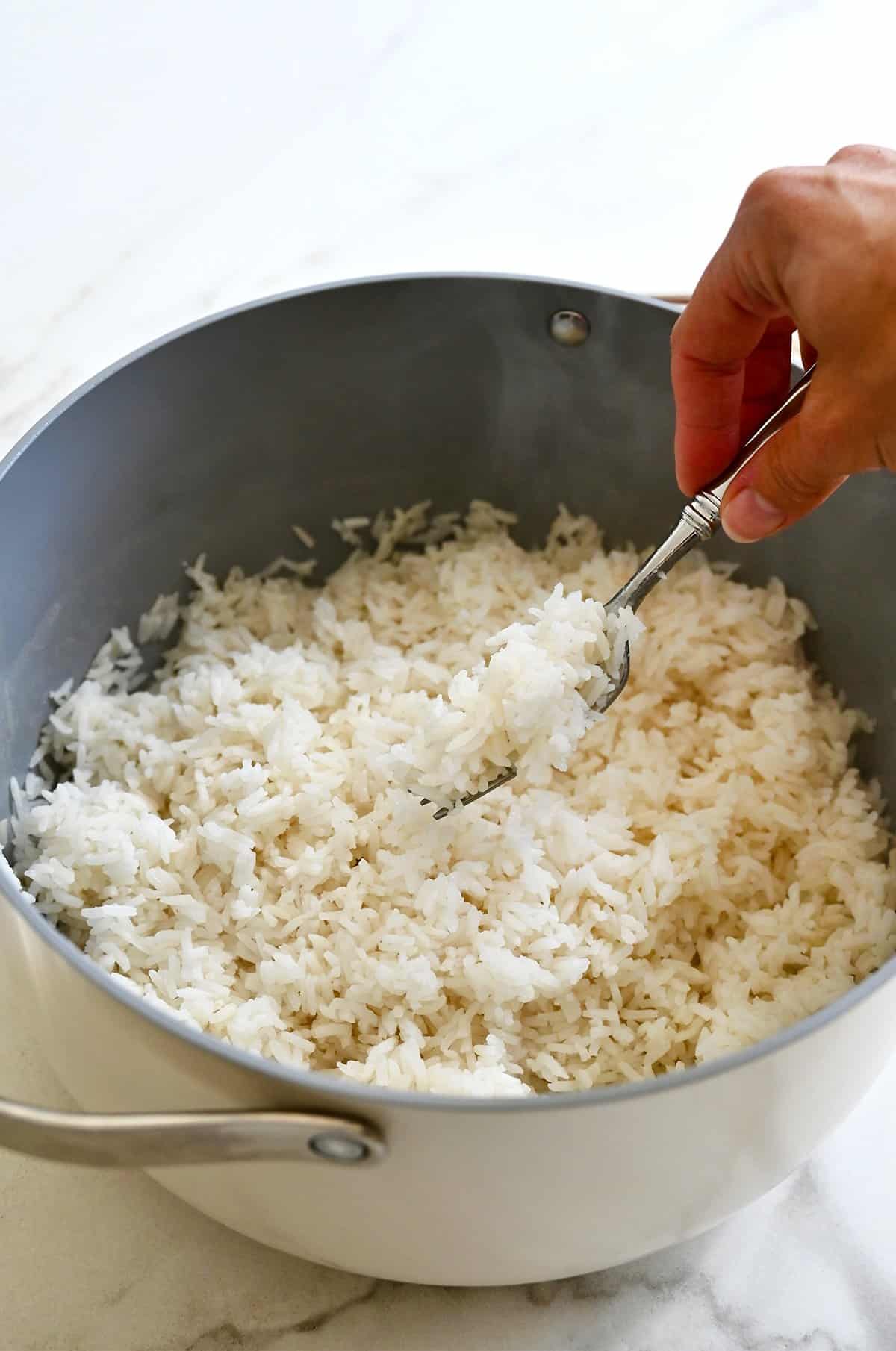 Fluffing cooked white rice in a pot with a fork.
