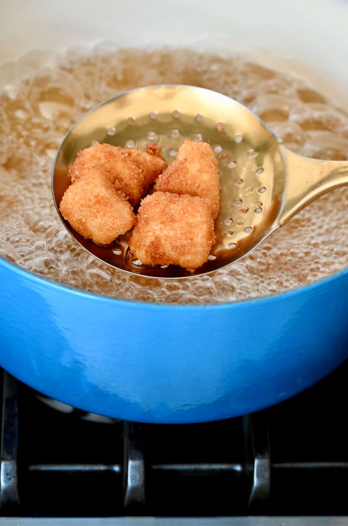 Fried chicken nuggets on a slotted spoon over a Dutch oven with hot oil.