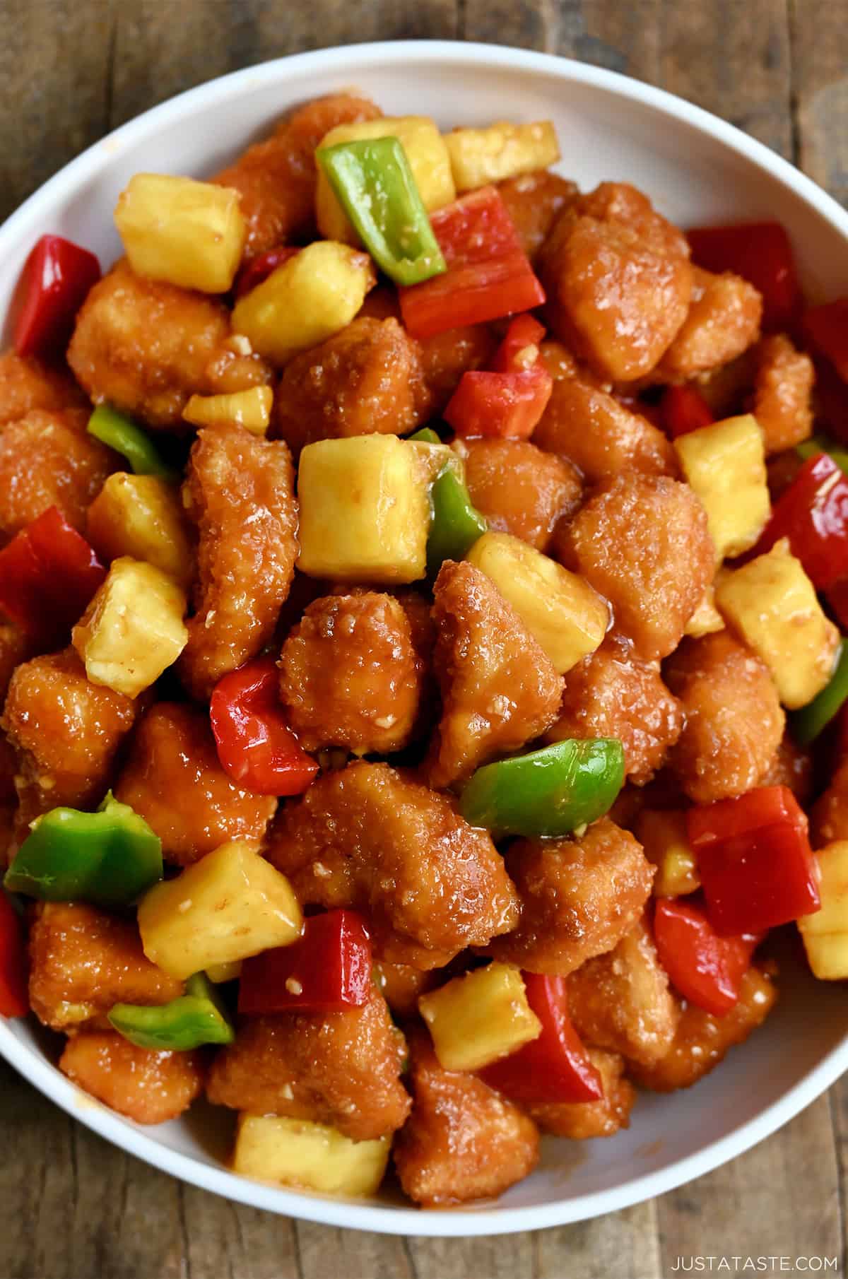 Homemade sweet and sour chicken with pineapple and bell peppers on a dinner plate.
