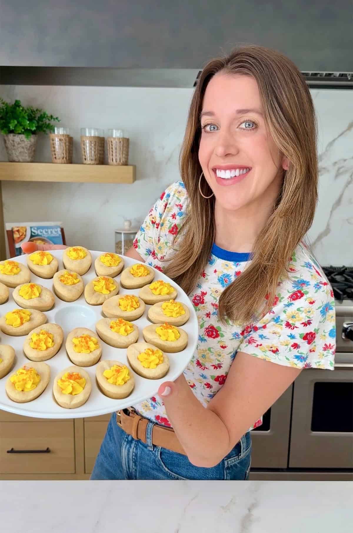 Kelly Senyei holds a tray of Easter sugar cookies with yellow frosting that look like deviled eggs.