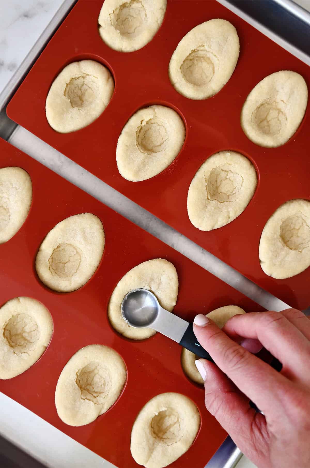 Pressing a ½ teaspoon measuring spoon into a warm sugar cookie cup to create space for frosting.