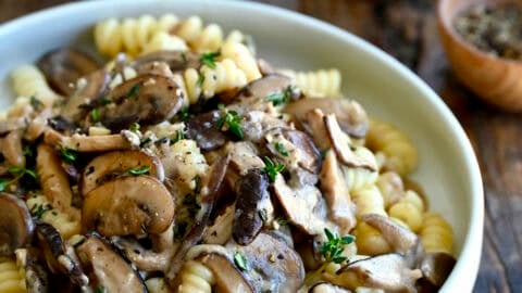 A bowl of creamy mushroom pasta with fusilli, garnished with fresh thyme and grated Parmesan.
