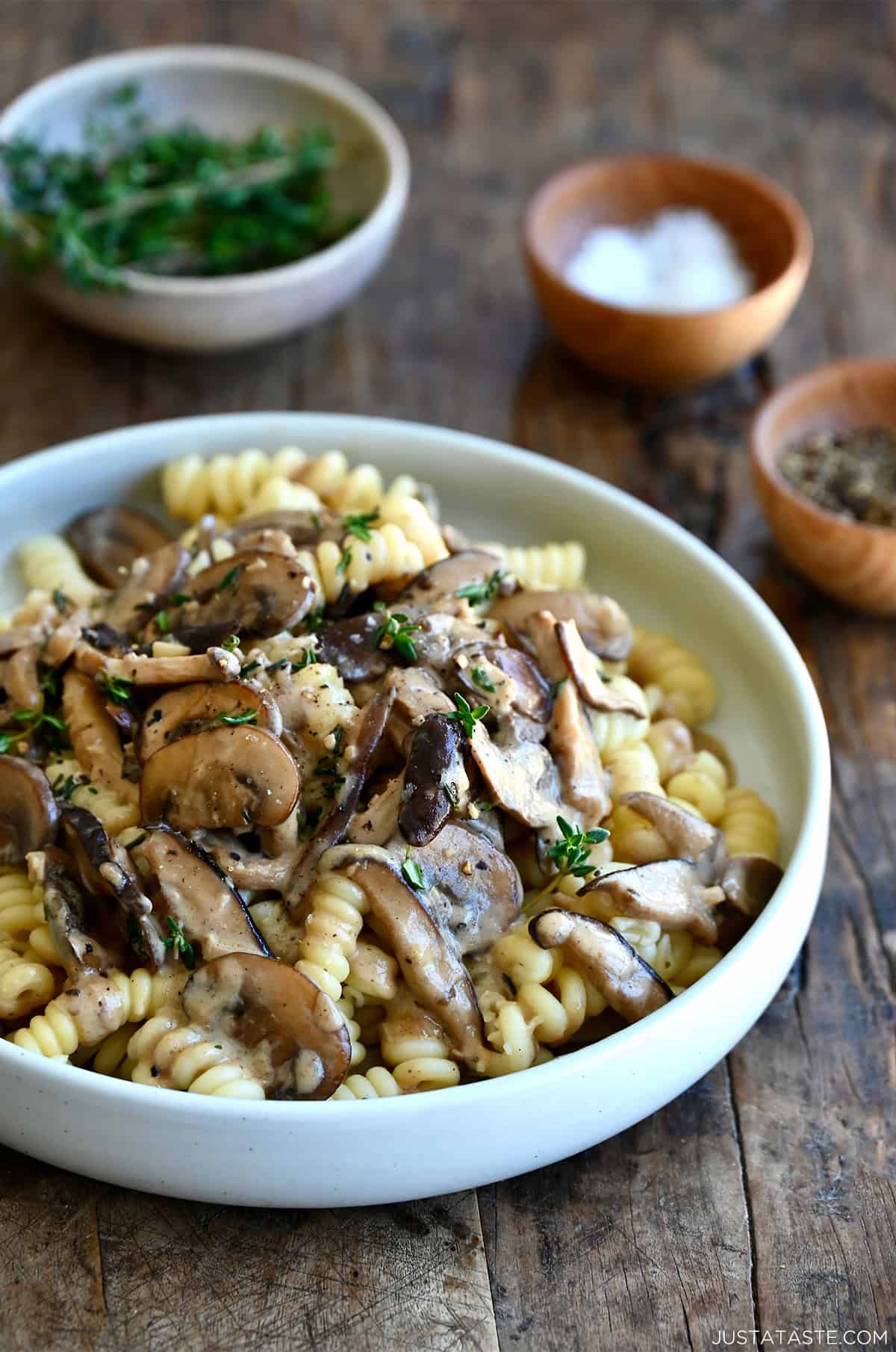 A bowl of creamy mushroom pasta with fusilli, garnished with fresh thyme and grated Parmesan.