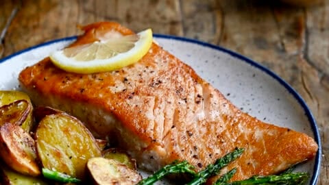 Pan seared salmon filet on a dinner plate with roasted asparagus and baby red potatoes.