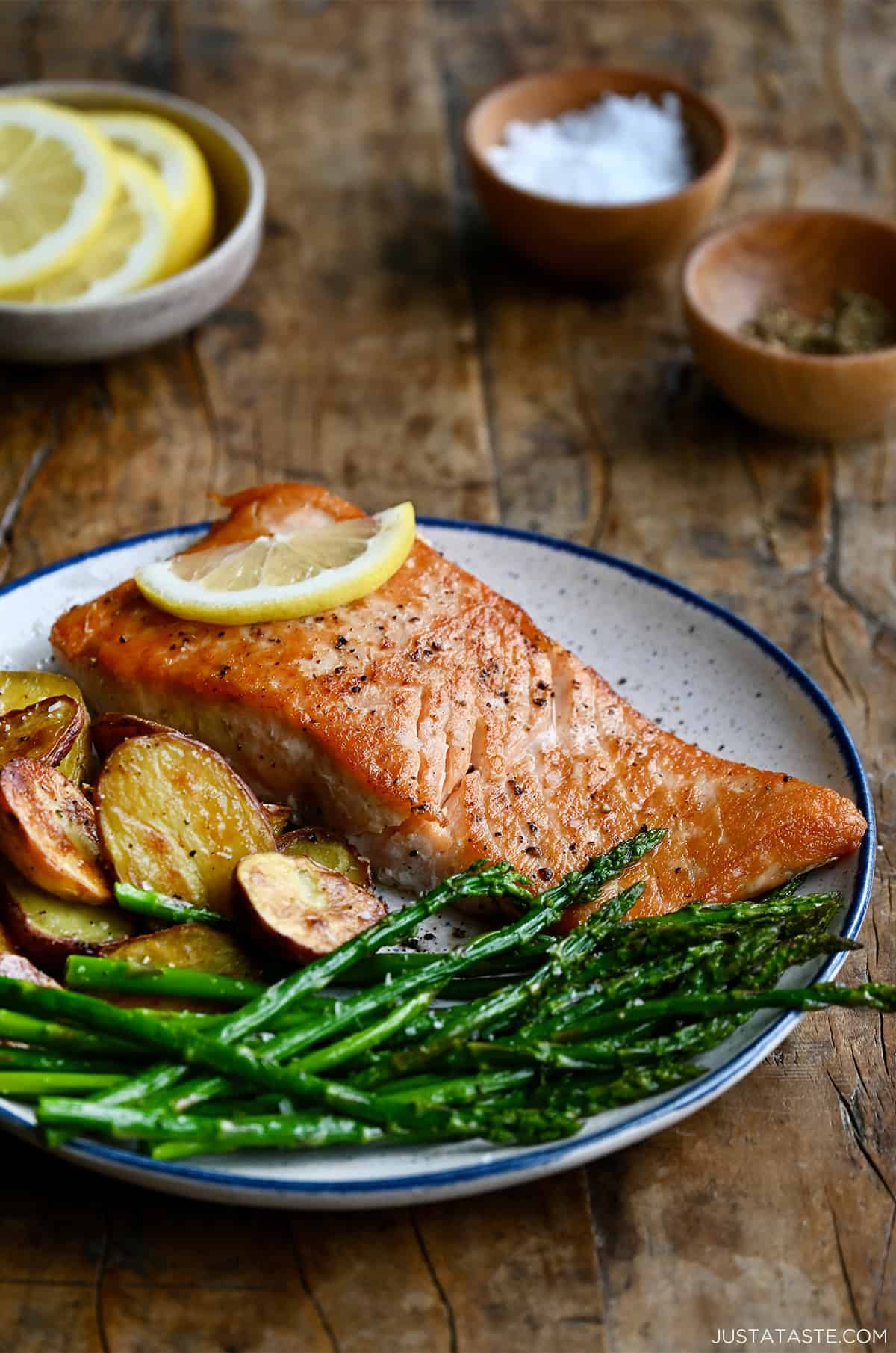 Pan seared salmon filet on a dinner plate with roasted asparagus and baby red potatoes.