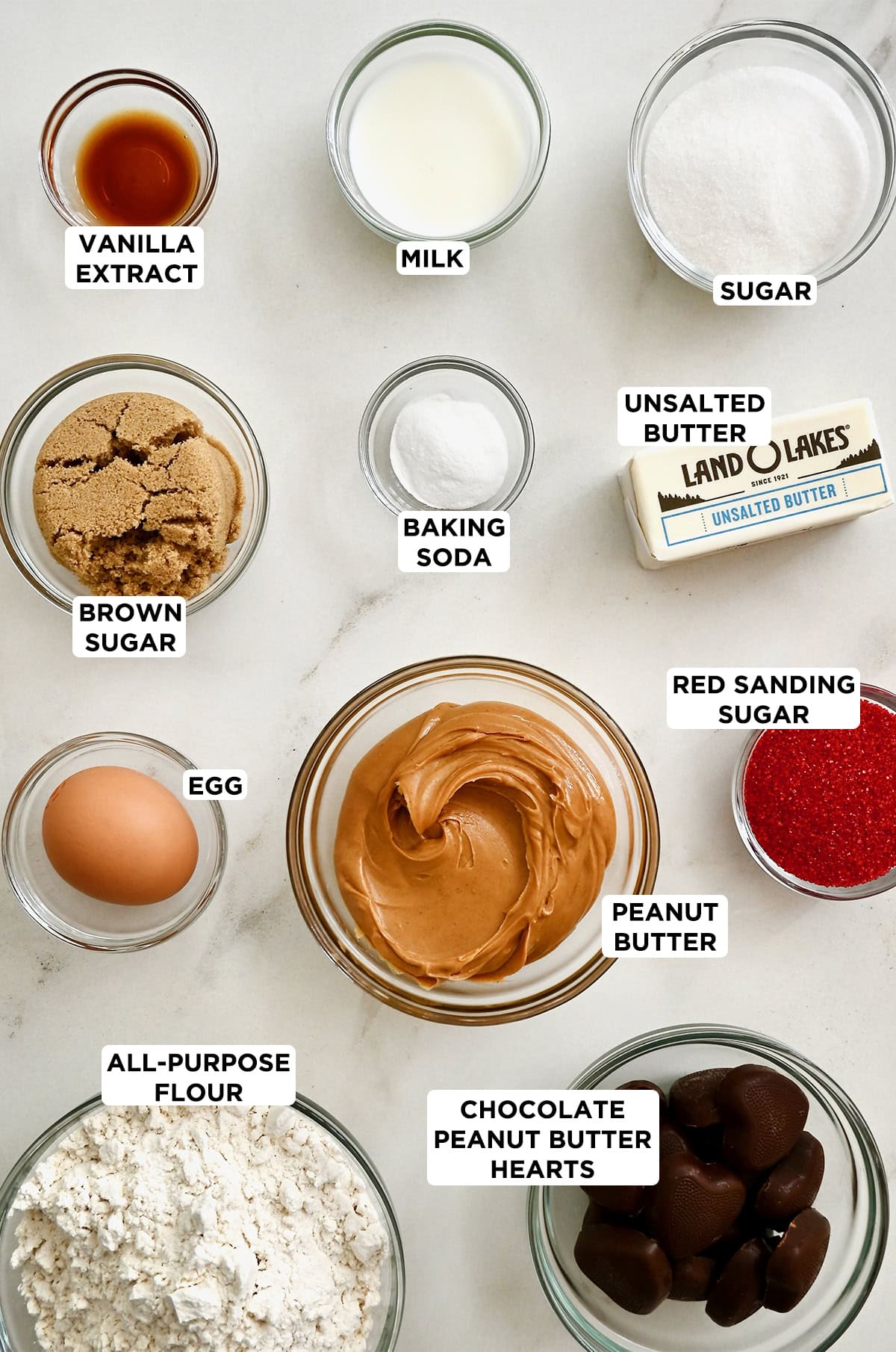 Various sizes of glass bowls containing all of the ingredients to make peanut butter heart cookies.