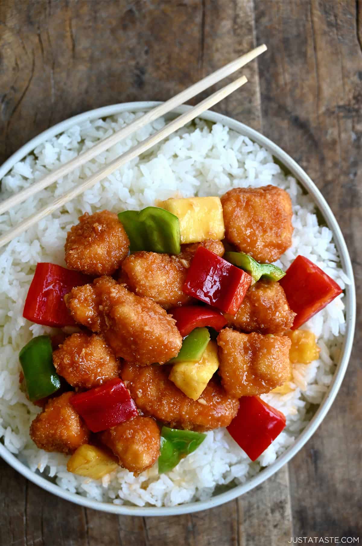 Sweet and sour chicken over white rice on a plate with chopsticks.