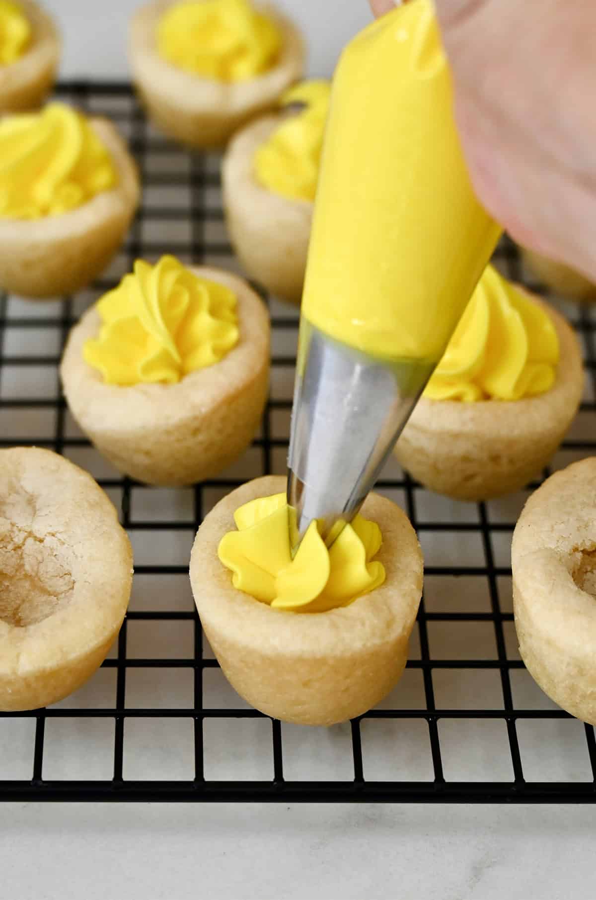 Piping yellow frosting into the center of baked sugar cookies.