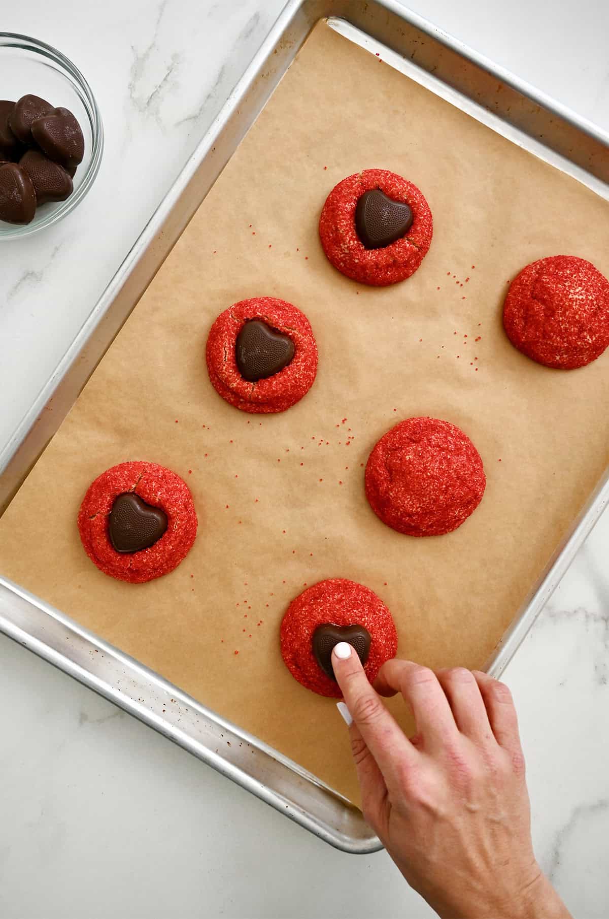 Pressing a Reese's Peanut Butter Heart into the center of a freshly baked peanut butter cookie coated in red sanding sugar.