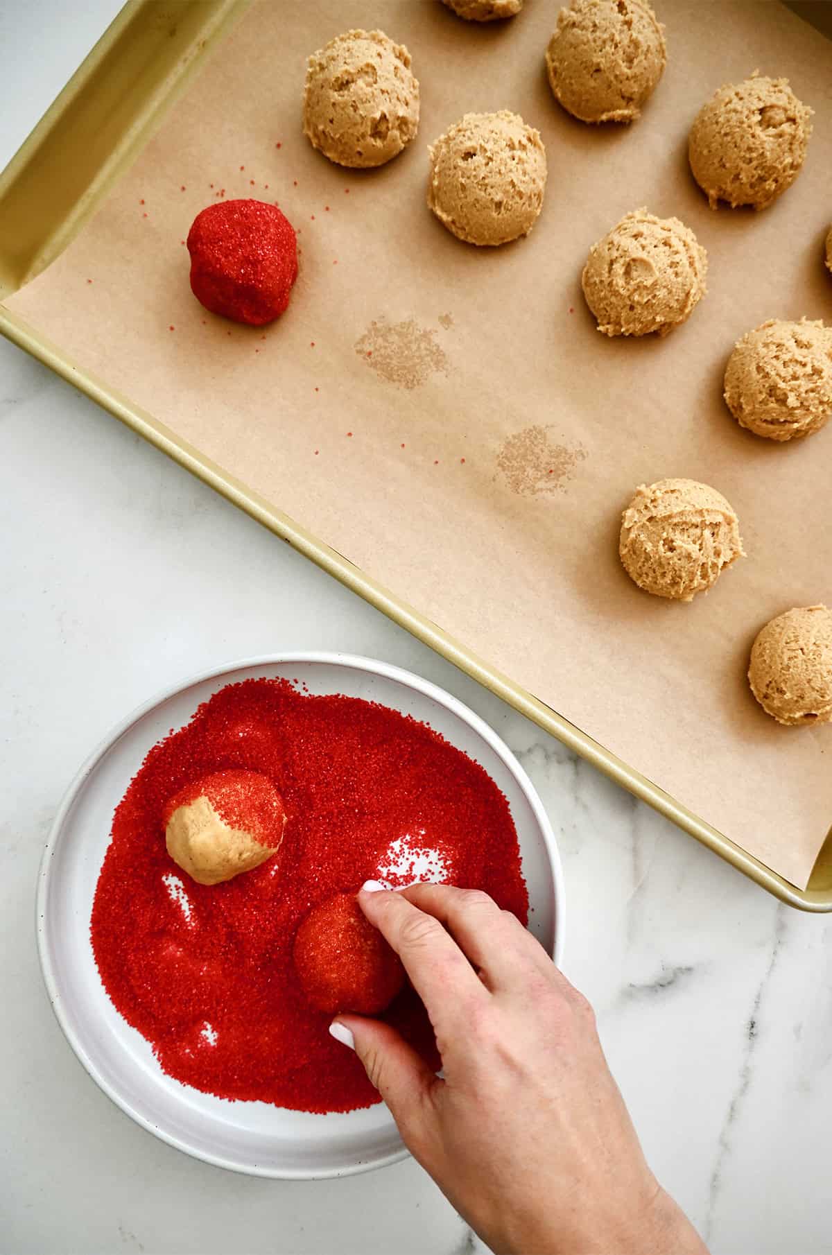 Rolling peanut butter cookie dough in red sanding sugar to make heart cookies.