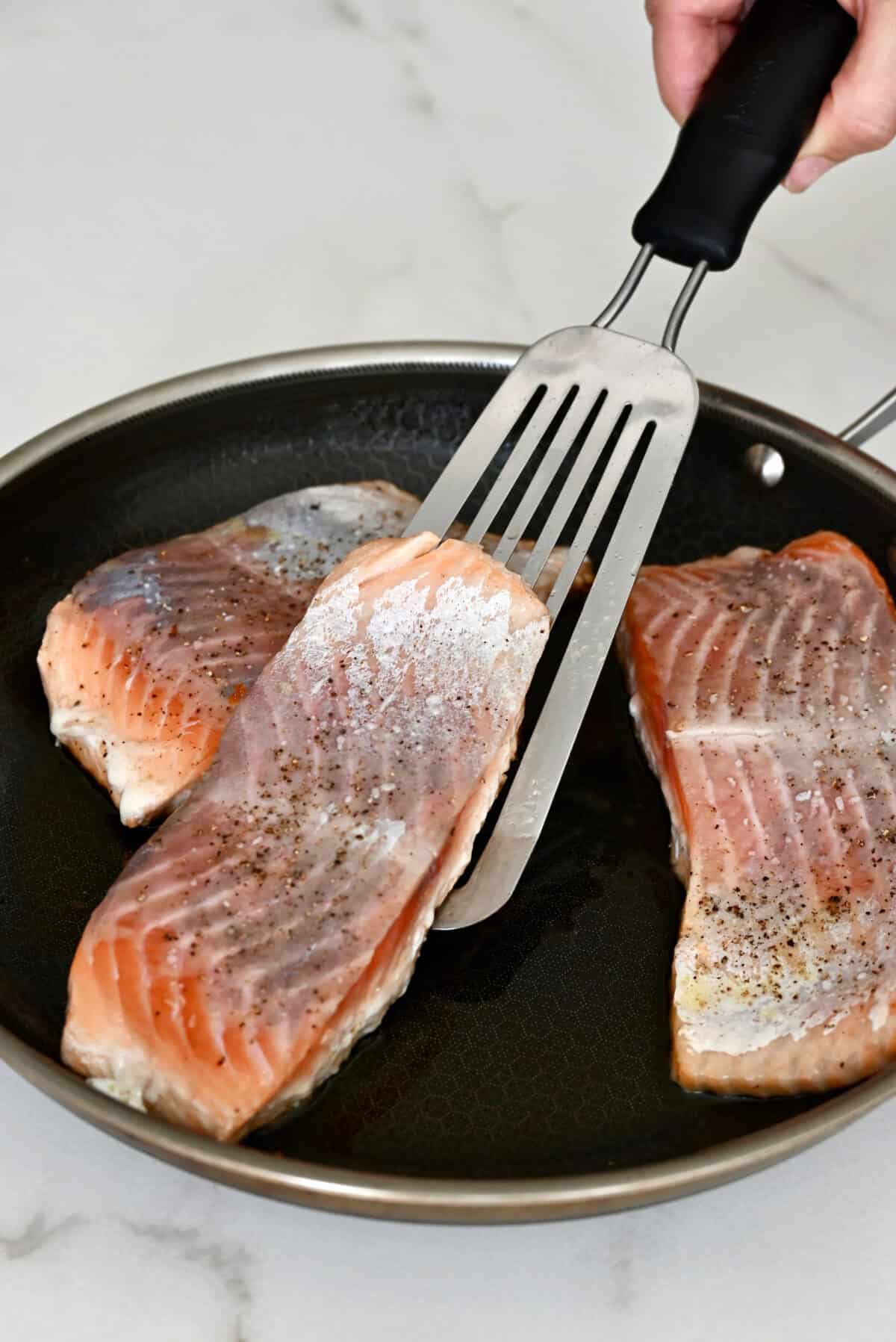 Using a fish spatula to flip salmon in a skillet to sear the second side.