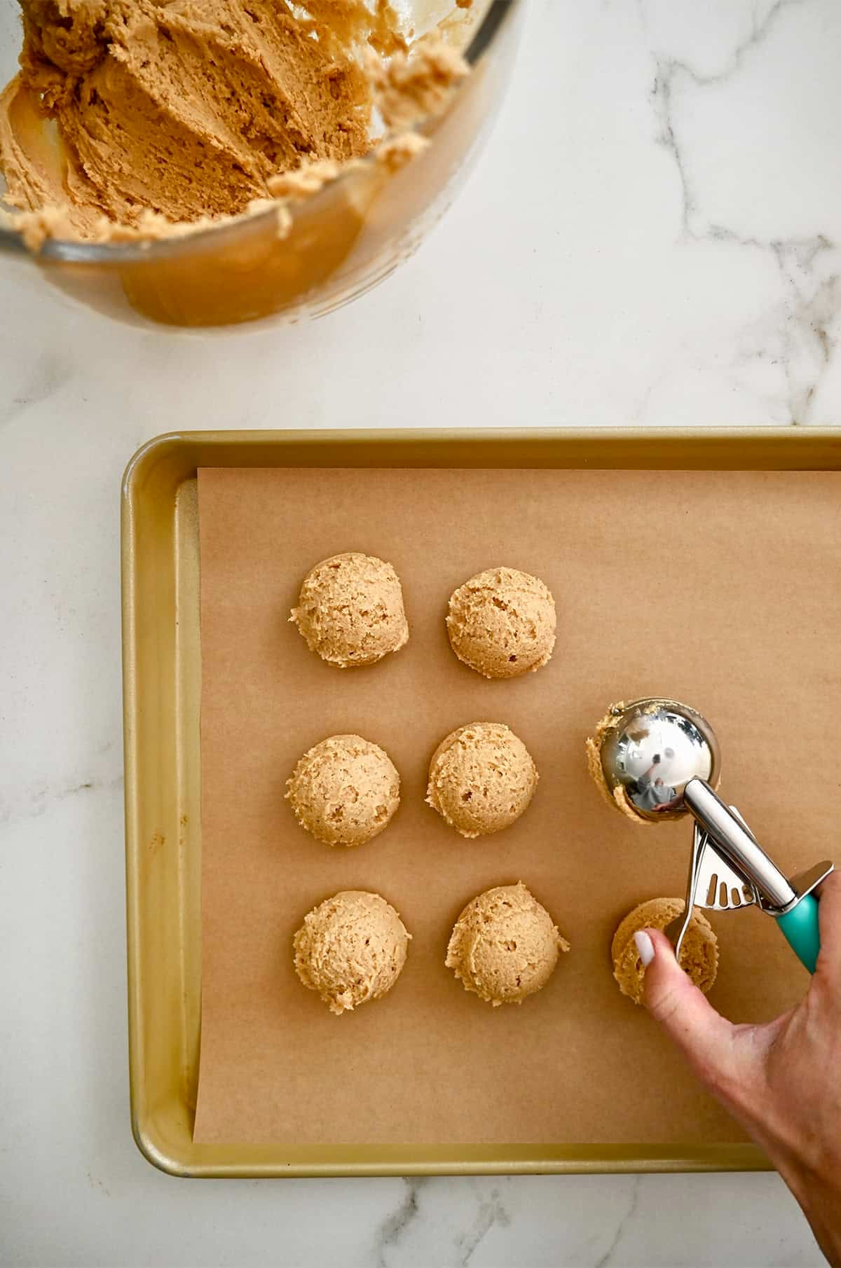 Scooping balls of peanut butter dough onto a parchment paper-lined baking sheet.